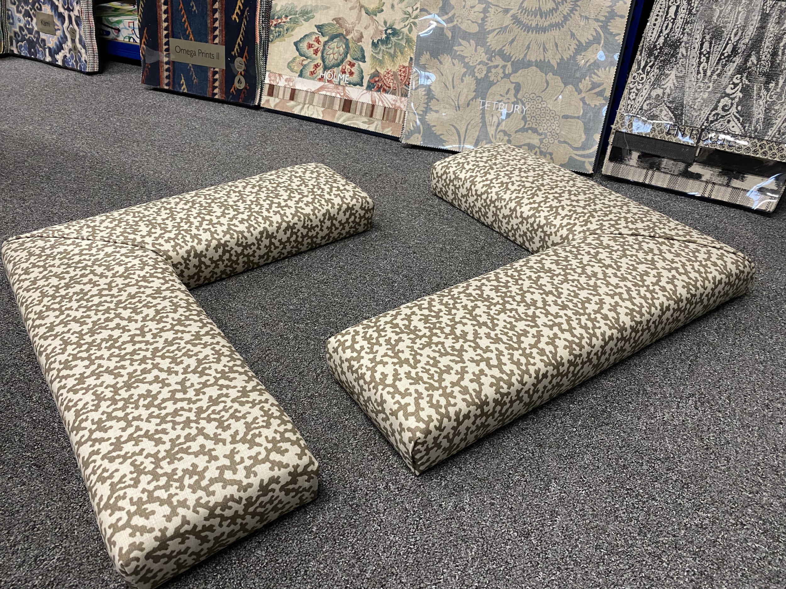 A pair of fireplace fender seats upholstered in pattern fabric laid out on a floor with fabric sample books showing in the background.