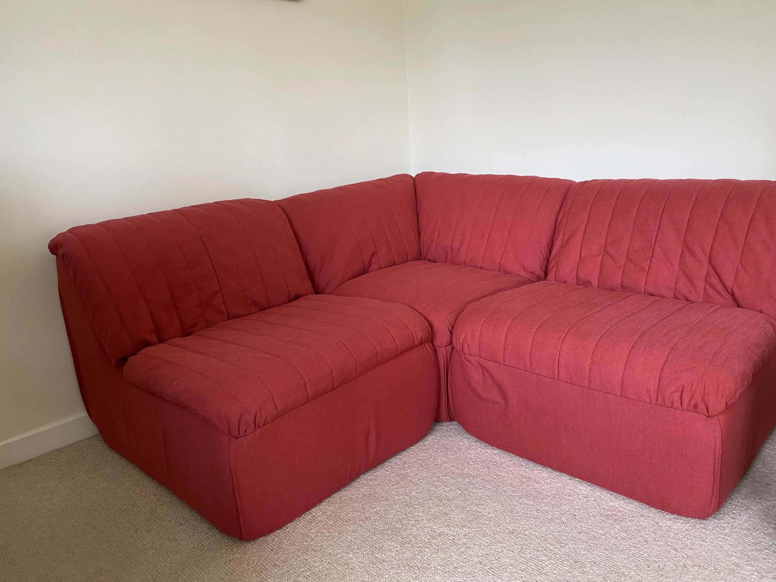Red sectional sofa in a room with beige carpet and light-colored walls.