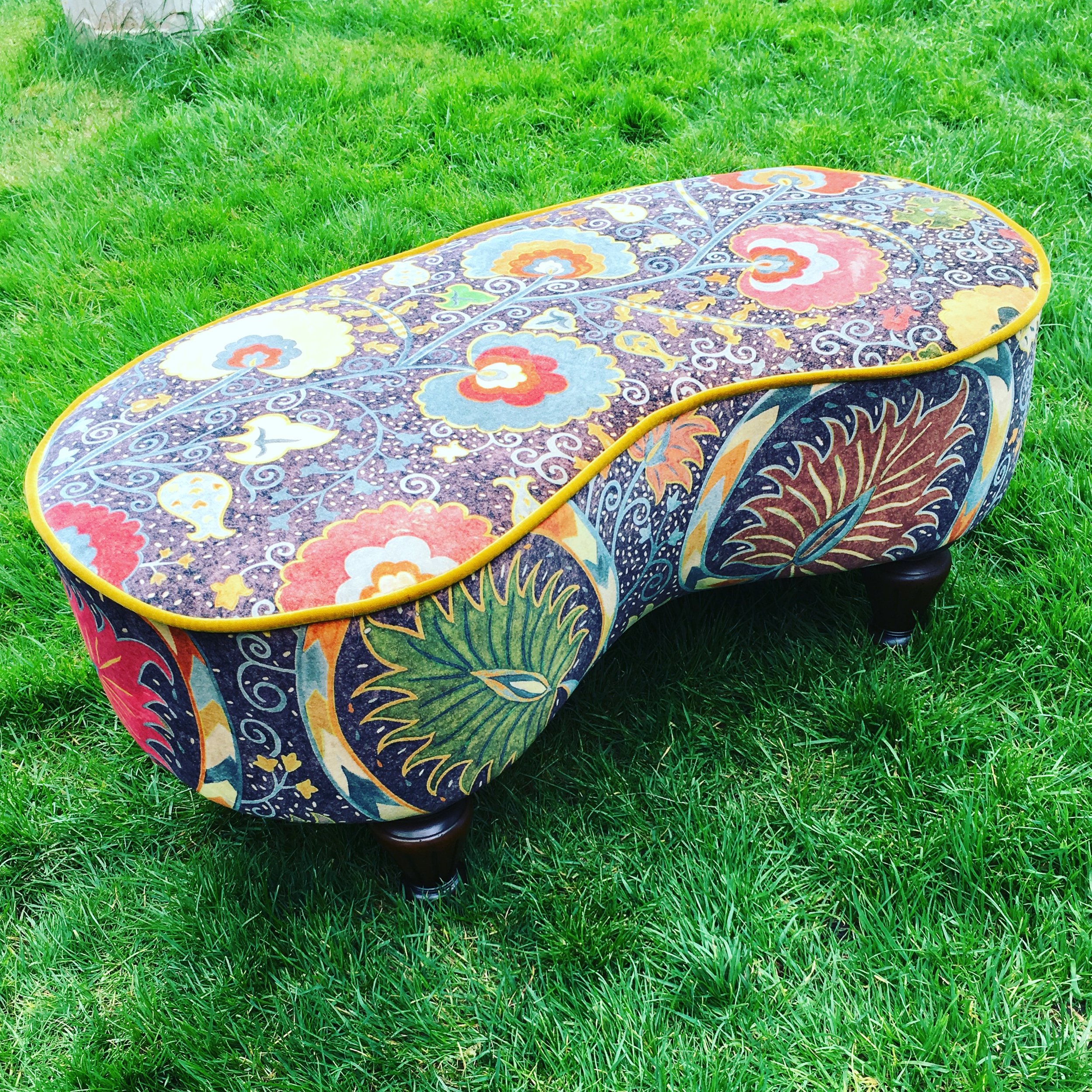 Colorful, patterned oval footstool with floral and abstract designs on a grassy lawn.