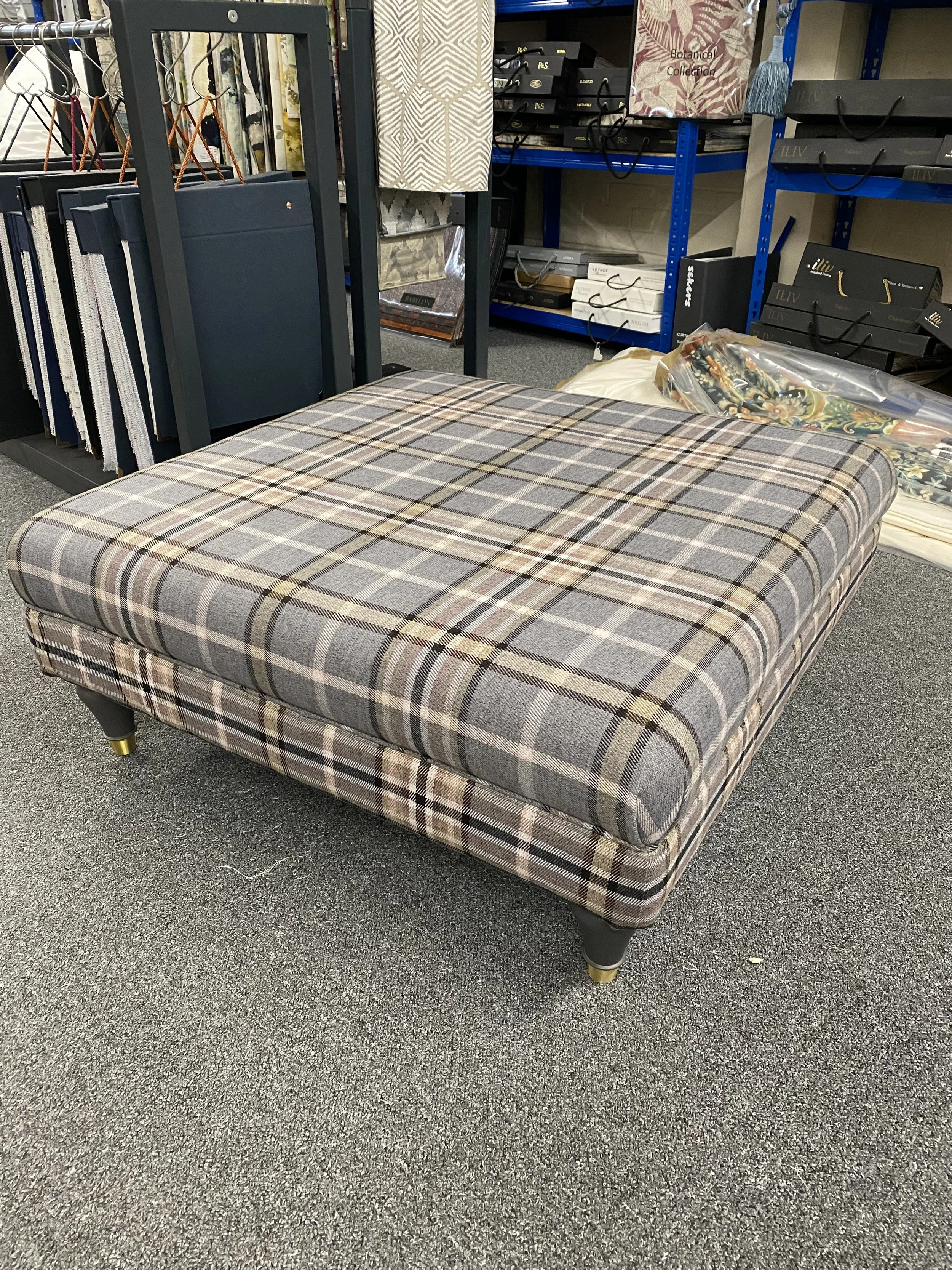 A checkered upholstered ottoman with a gray, beige, and brown pattern in a store setting.