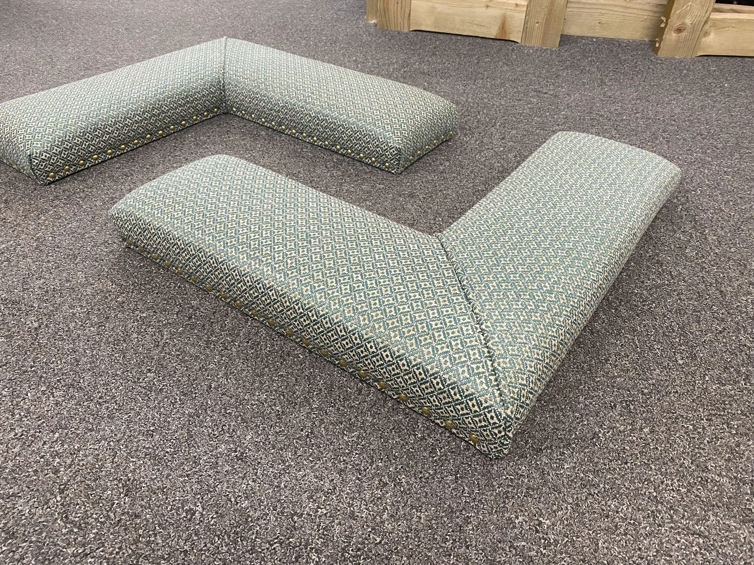 A pair of L shape fireplace fender seats upholstered in green pattern fabric with decorative nail trim shown on a great carpeted floor.