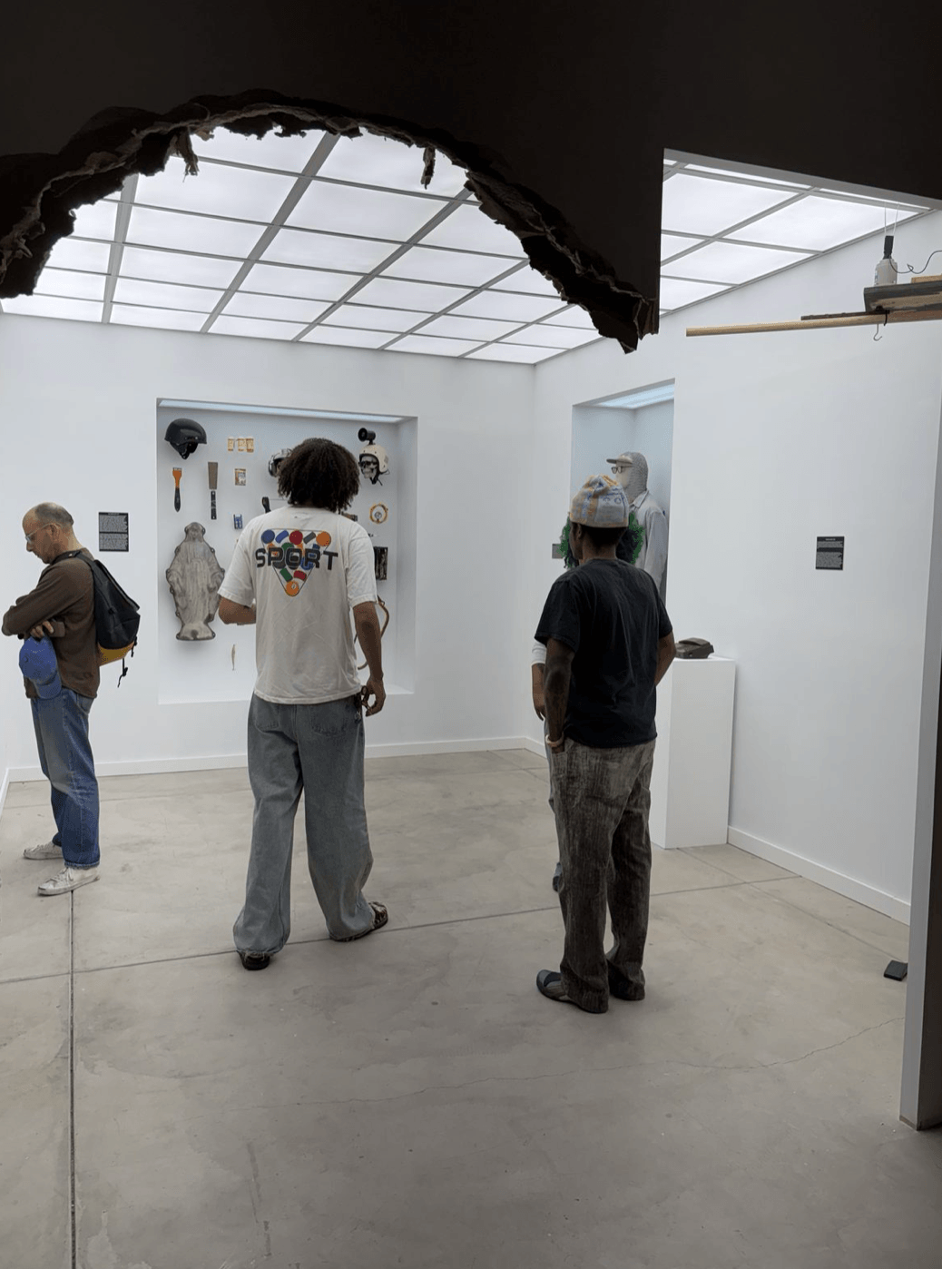 View into the constructed gallery through the broken drywall opening, with visitors.