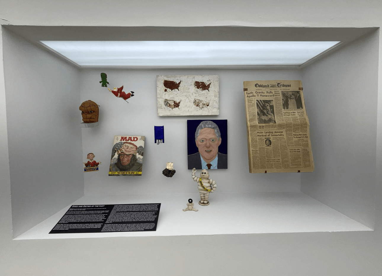  Inset Display, “Gods and Deities of the Past.” Includes a painted portrait of Bill Clinton, a 1969 Oakland Tribune, a MAD magazine, a Michelin Man figurine, and a painted panel of four United States maps. 