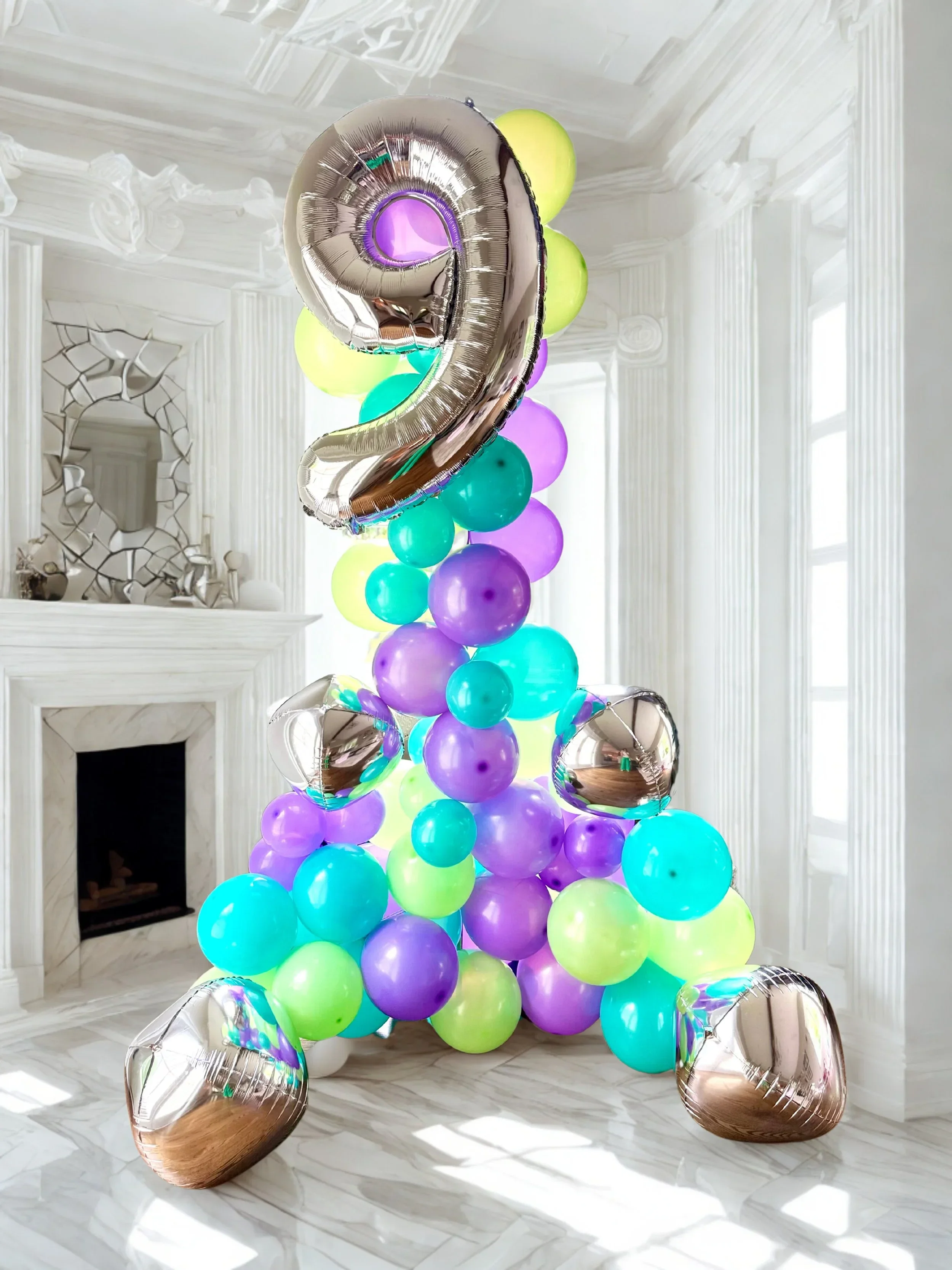Colorful balloon display in front of a white ornate room with a large mirror and a fireplace.