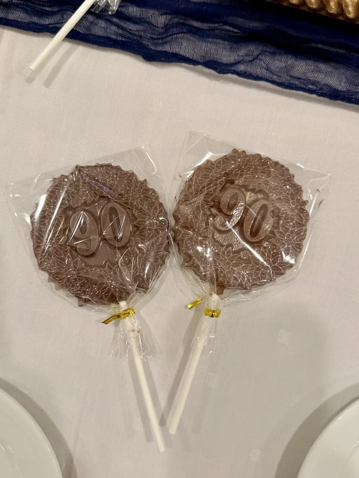 Two chocolate lollipops with the number 50 on each, wrapped in clear plastic and placed on a table.