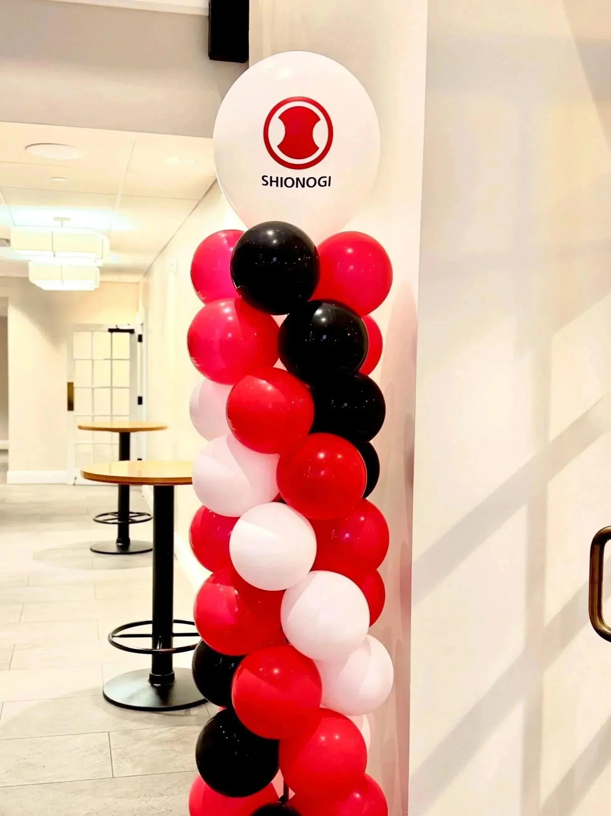 A column of balloons in red, black, and white colors, with a white round sign on top featuring a red logo and the word 'SHIONGI' beneath it.