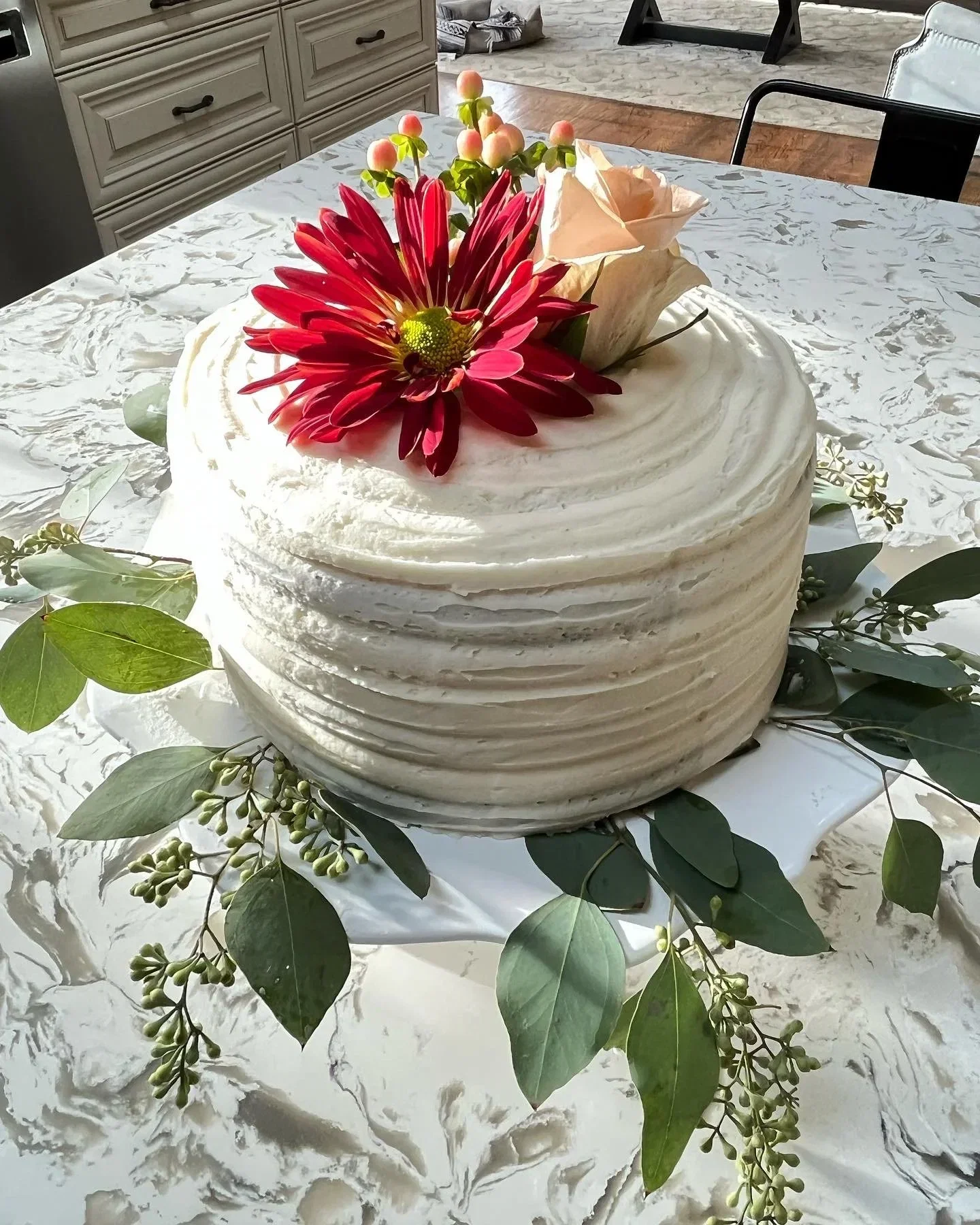 Decorative flower arrangement on a table with a white textured tablecloth, featuring a large red flower, beige roses, and greenery