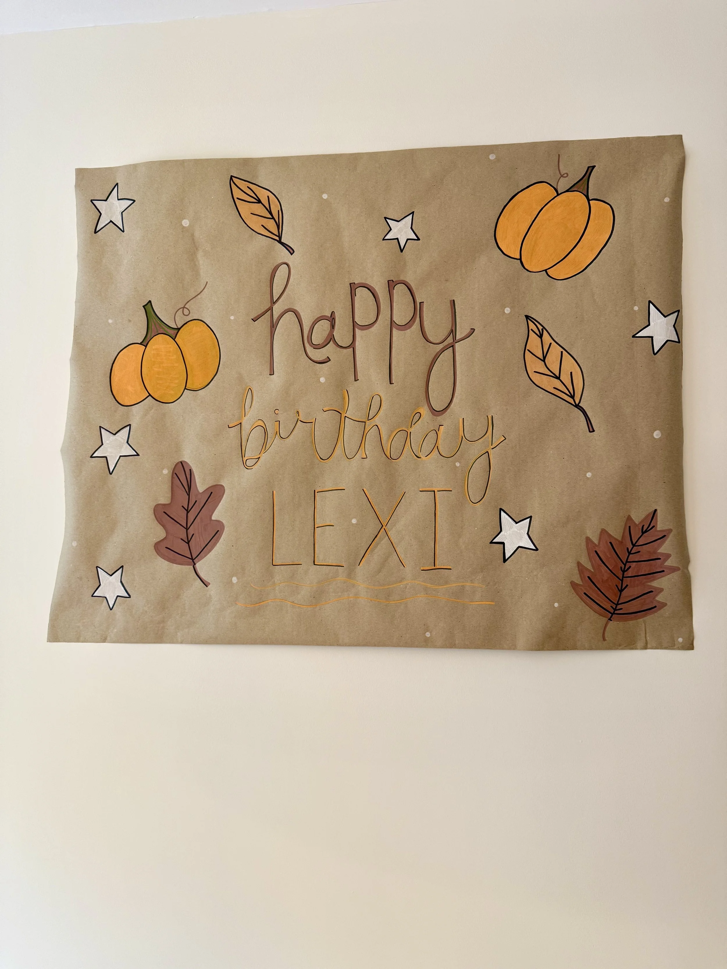 Decorative paper poster with autumn-themed drawings of pumpkins, leaves, stars, and the message "happy birthday LEXI" written in cursive.