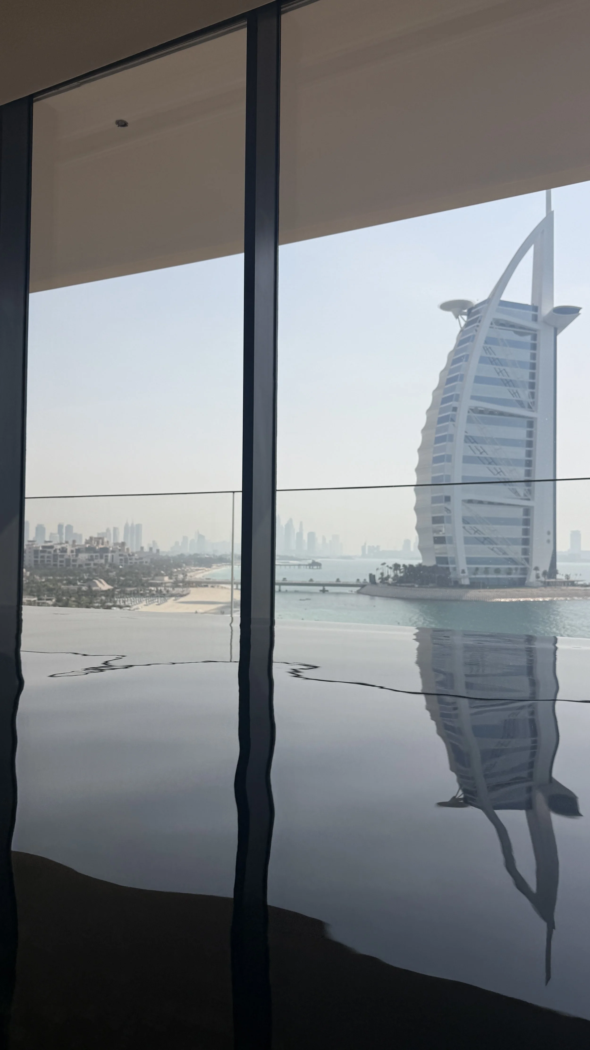 View of the Burj Al Arab hotel through window with curtains, featuring a water reflection.