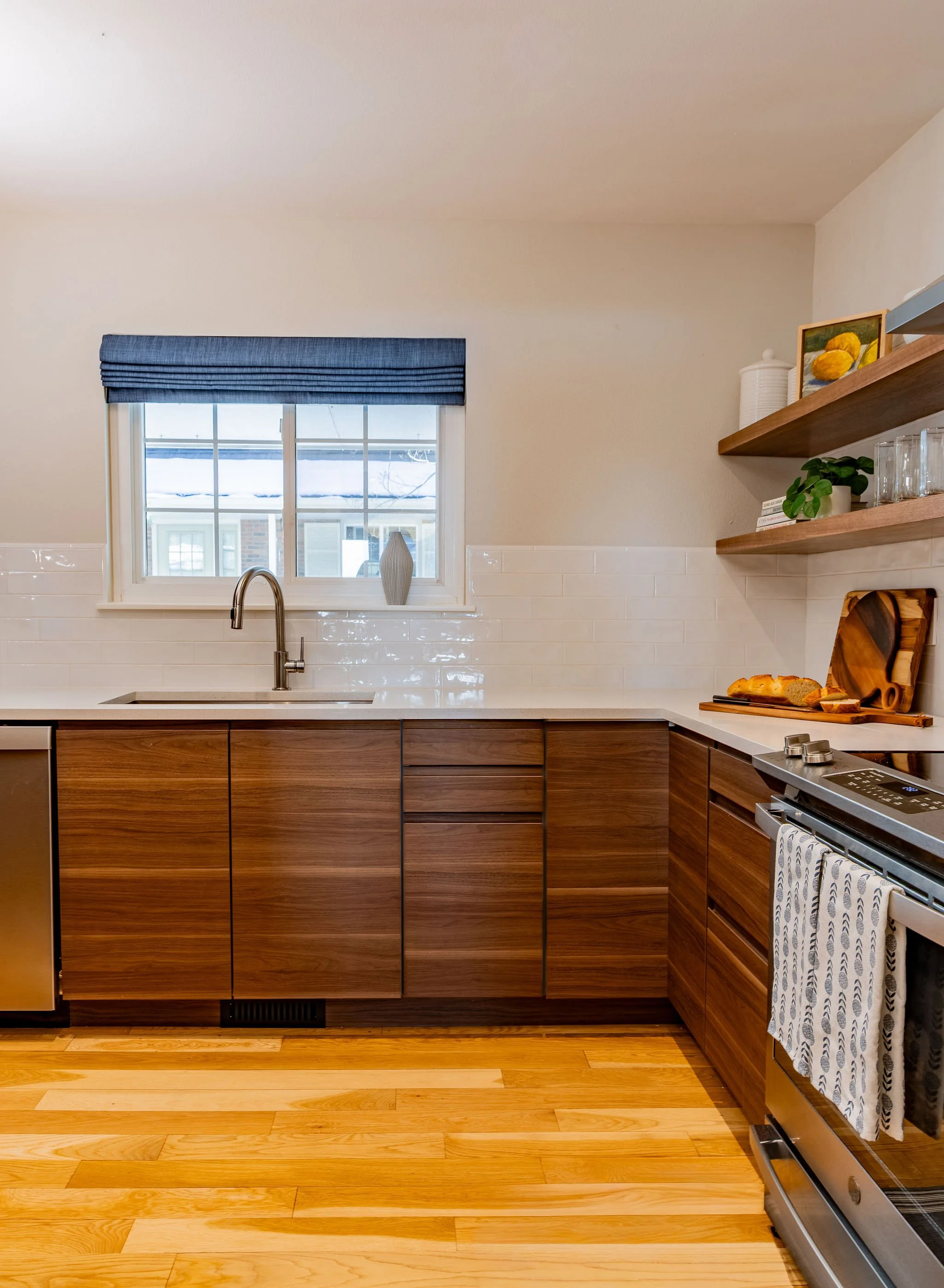 Tile feature wall wraps around under the kitchen window dressed with a blue roman shade tying into the overall color palette.