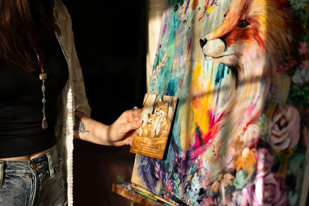 A person holding a trading card with an illustrated fox in front of a colorful, abstract painting of a fox.