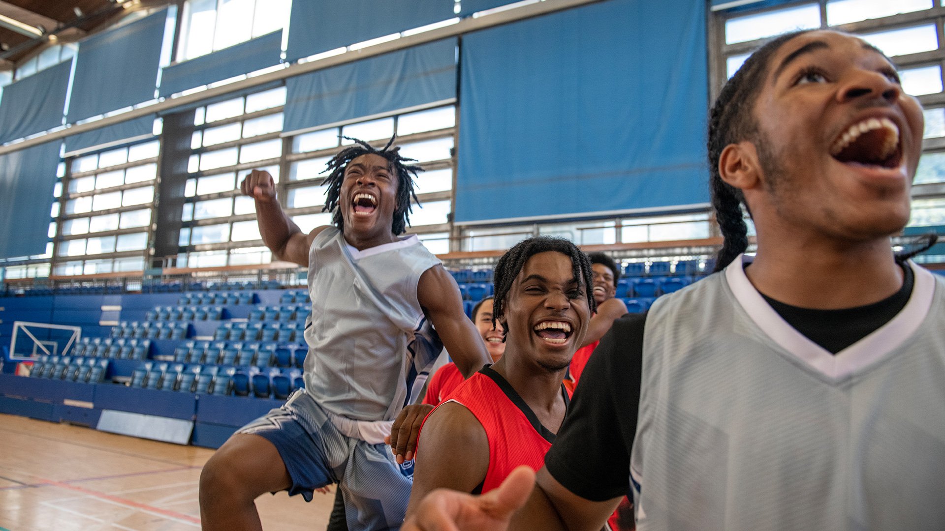 Group of smiling young basketball players celebrating in an indoor gymnasium.