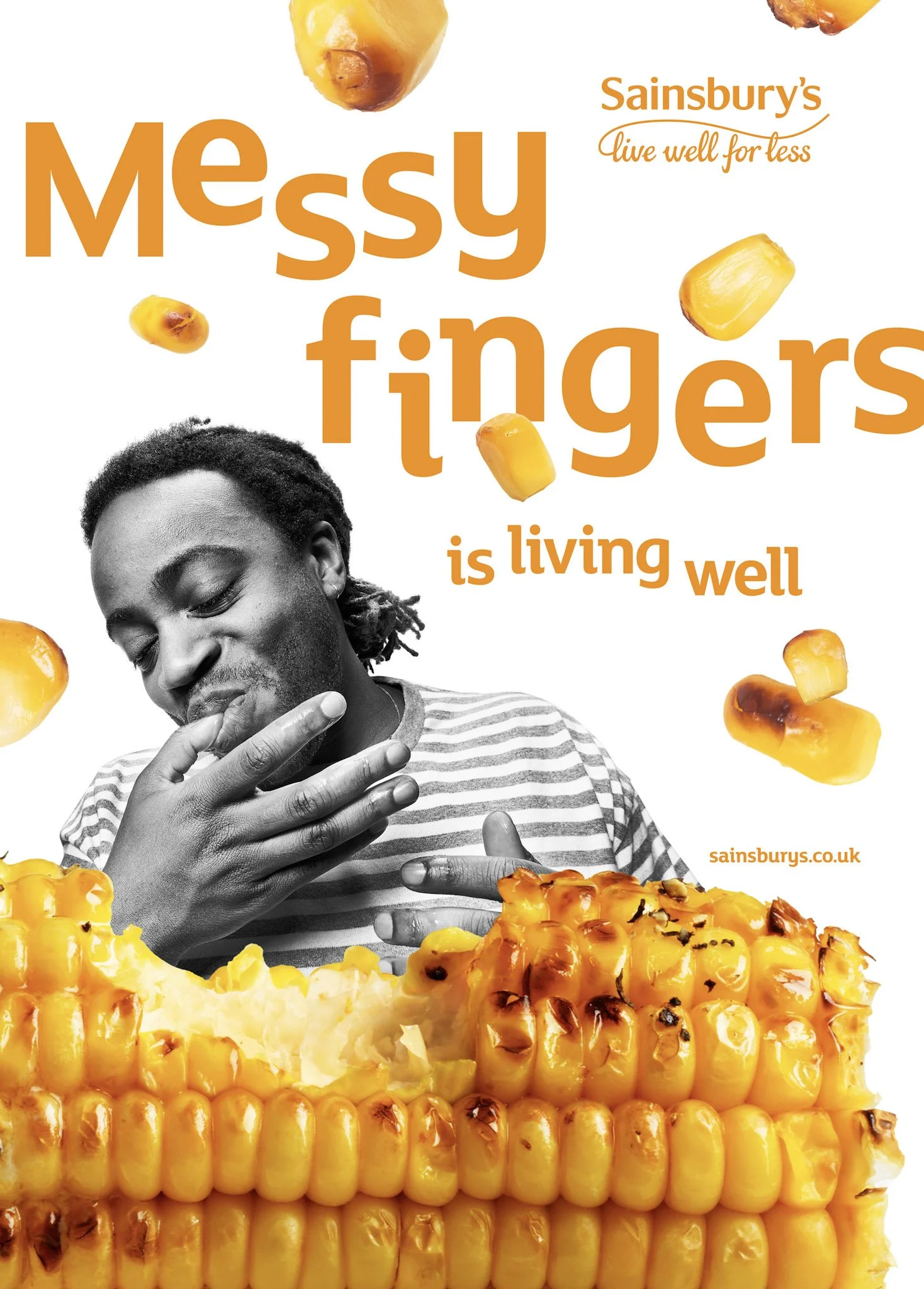 A Sainsbury's advertisement featuring a black and white photo of a man smelling his fingers, with bright yellow grilled corn on the cob and scattered corn kernels surrounding him, alongside orange text that reads 'Messy fingers is living well'.