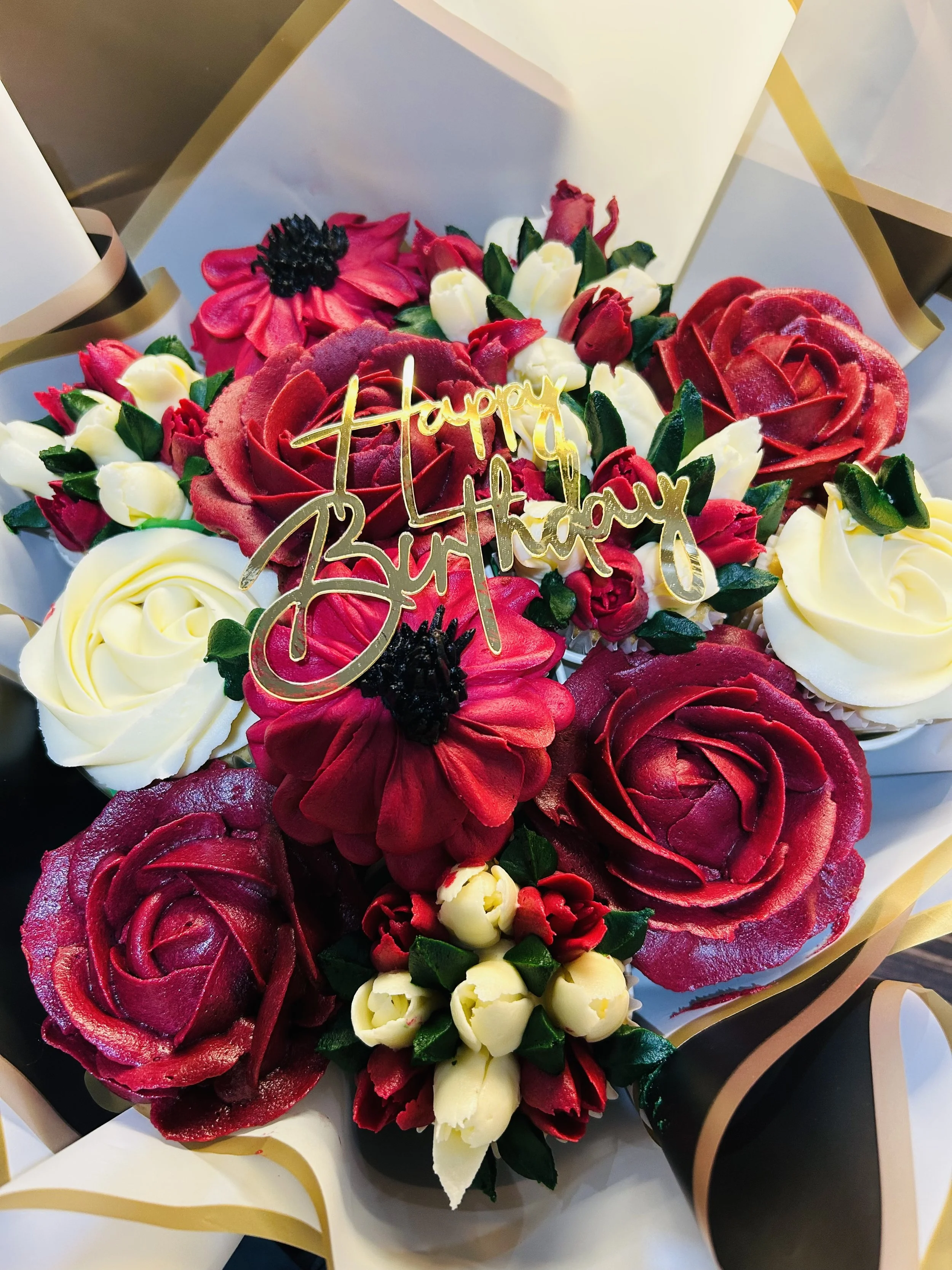 A bouquet of red and white flowers with green leaves, and a gold 'Happy Birthday' message in the center, wrapped in elegant white and gold wrapping paper.