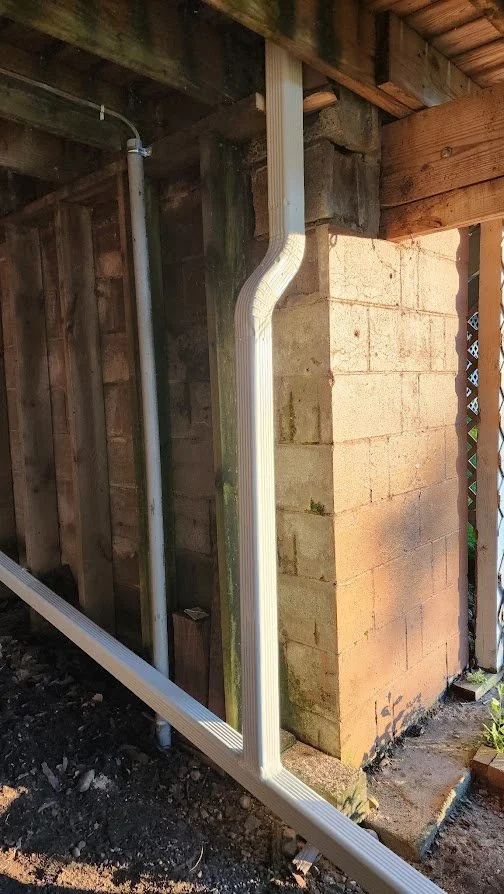 White plastic downspouts attached to the corner of a brick and wooden house exterior.