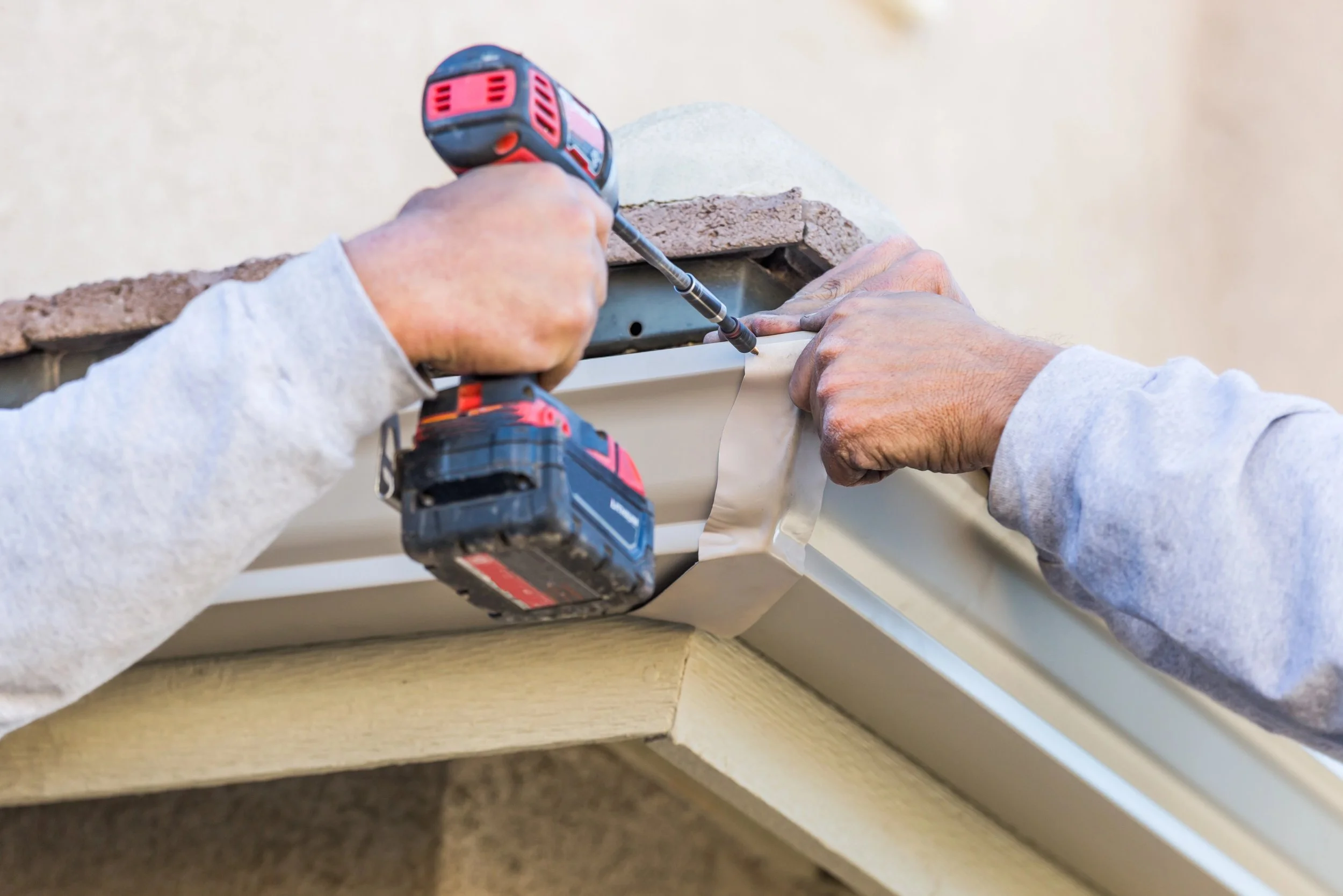 Person using a cordless drill to install or repair a gutter on the edge of a roof.