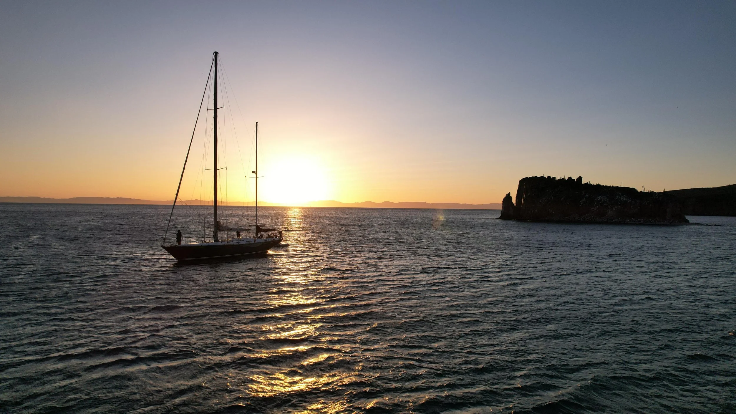 A sailboat on calm water during sunset with a small island in the distance.