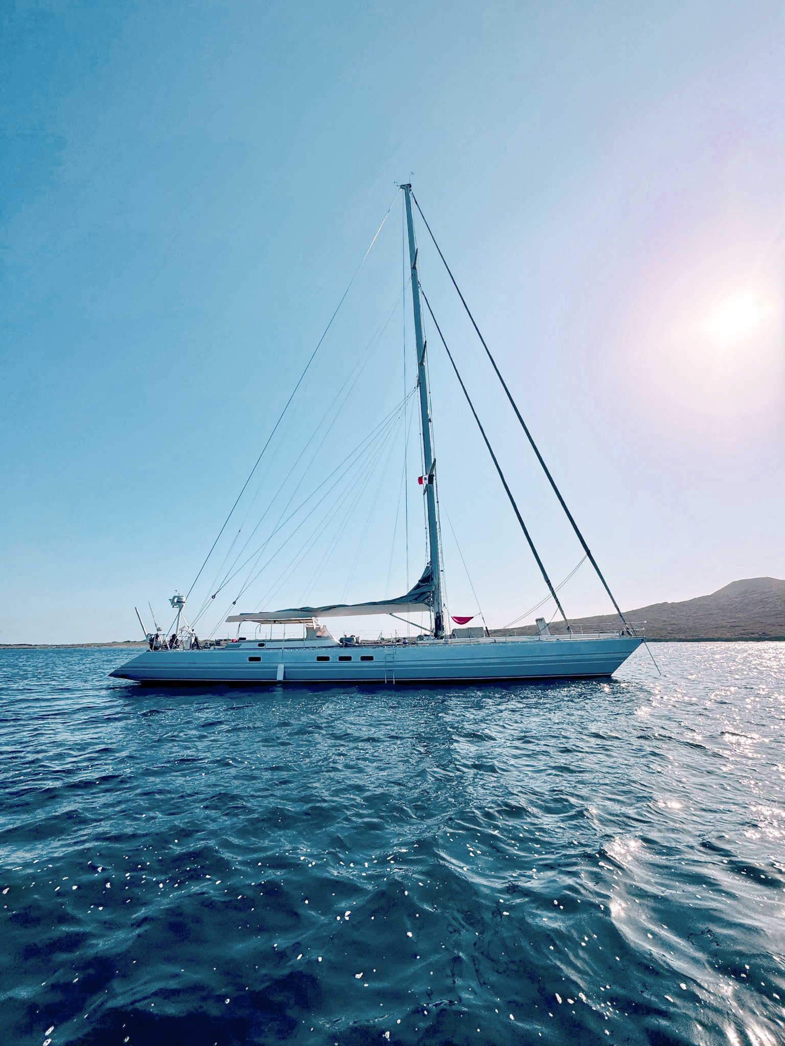 Sailboat on calm ocean waters with distant coastline under clear sky.