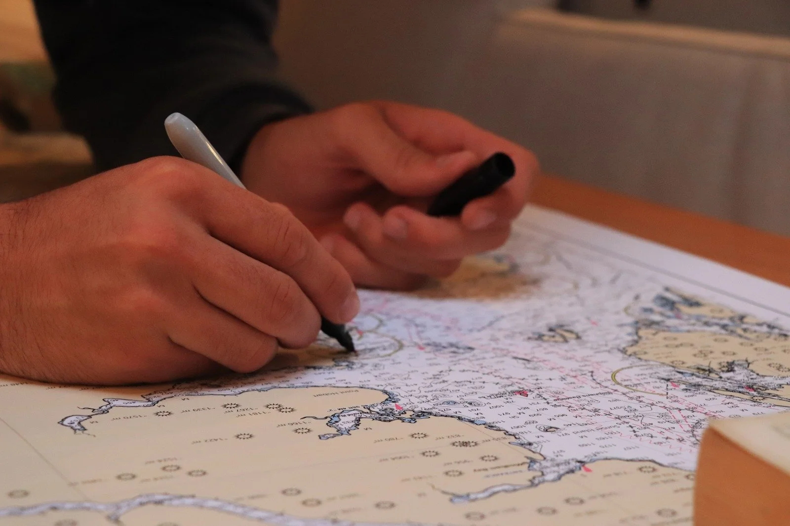 Person writing with a black marker on a nautical chart or map of a coastal area.