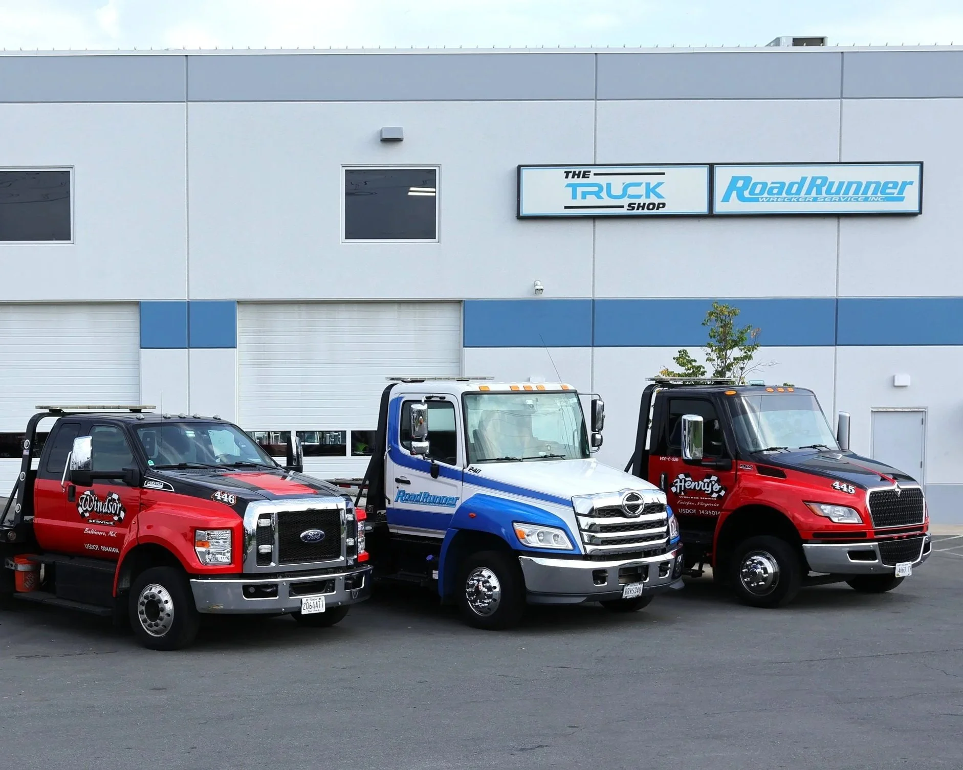 Three tow trucks parked in front of a building with signs reading ‘The Truck Shop’ and ‘Road Runner’
