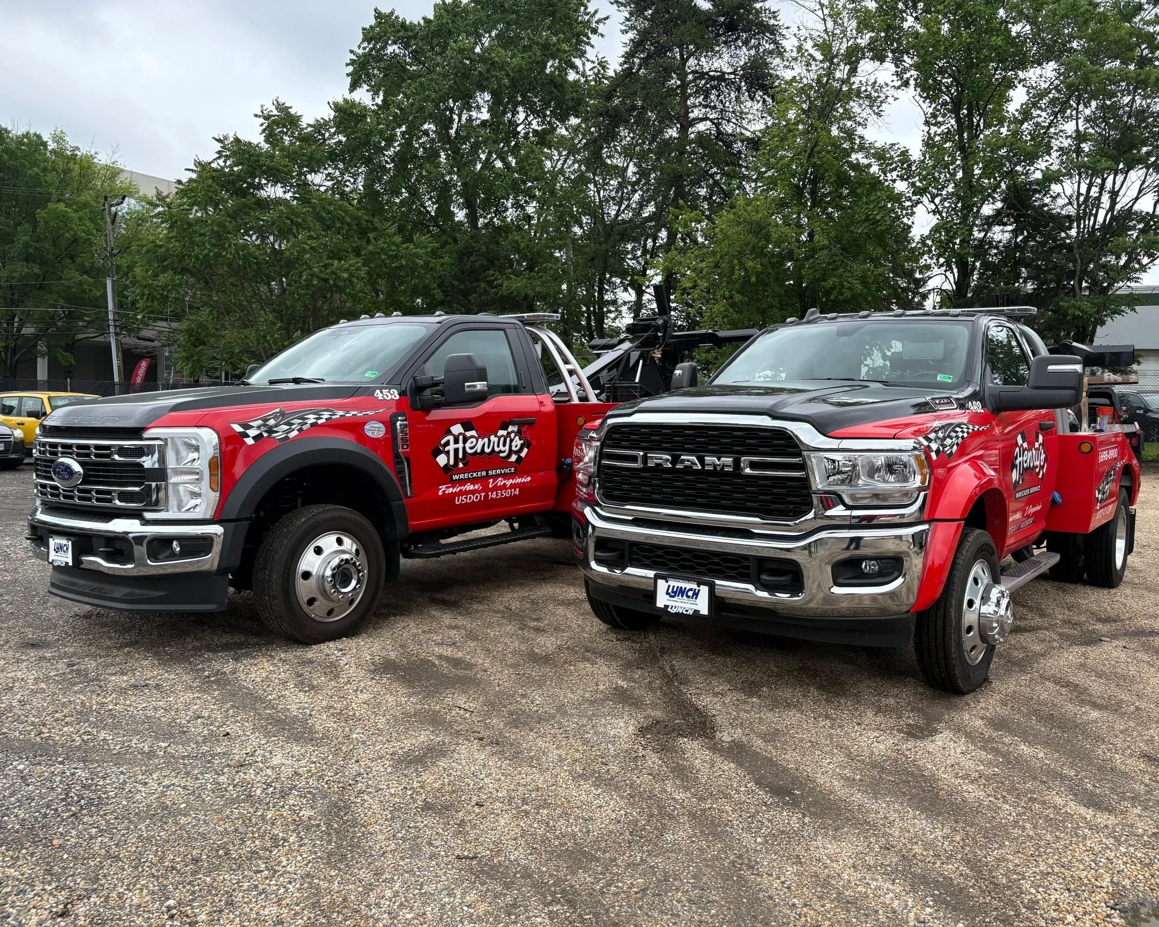 Two service trucks with red and black coloring and racing stripe designs parked on a gravel lot, with trees in the background.