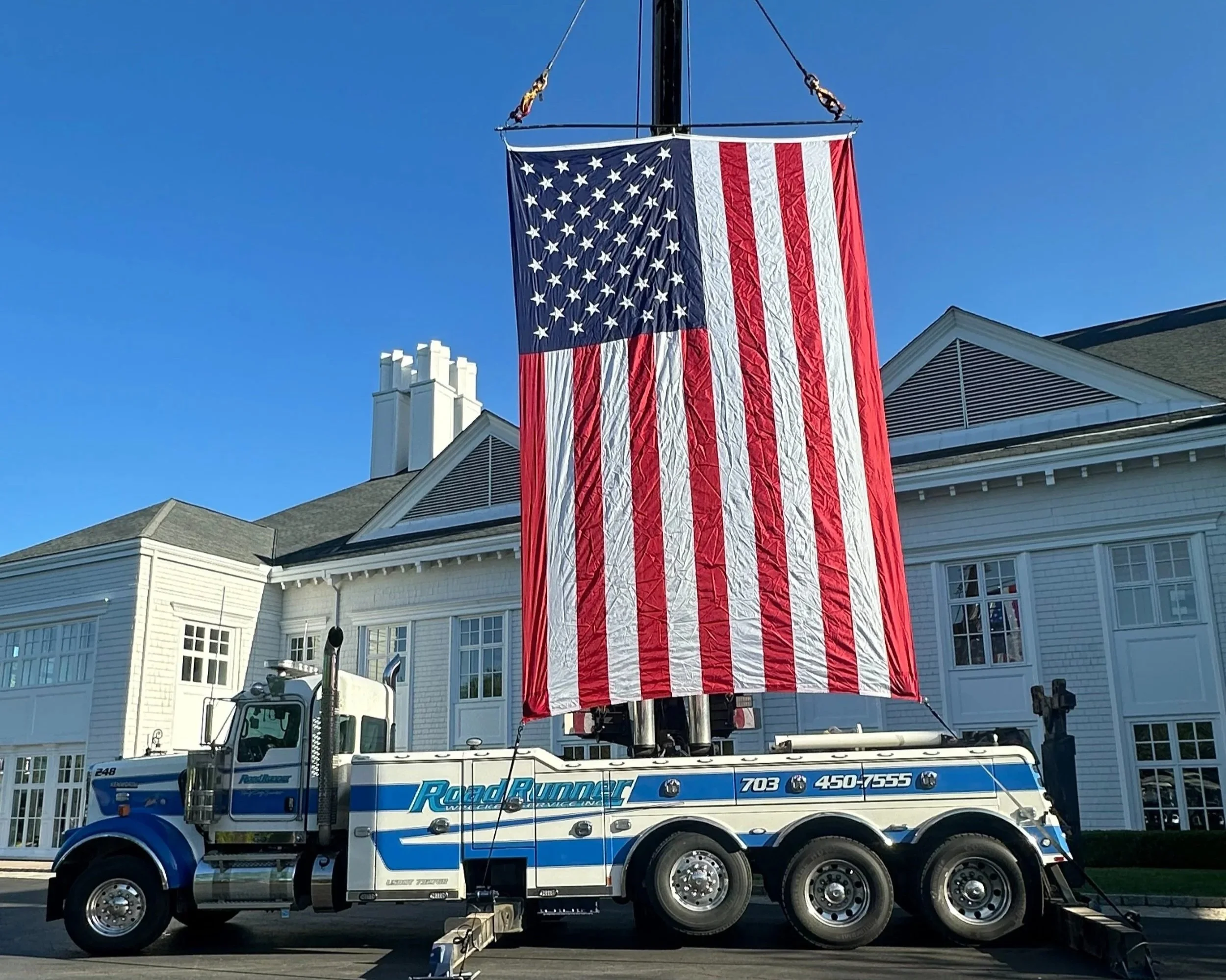 A large American flag displayed on a fire truck with a white building and blue sky in the background.