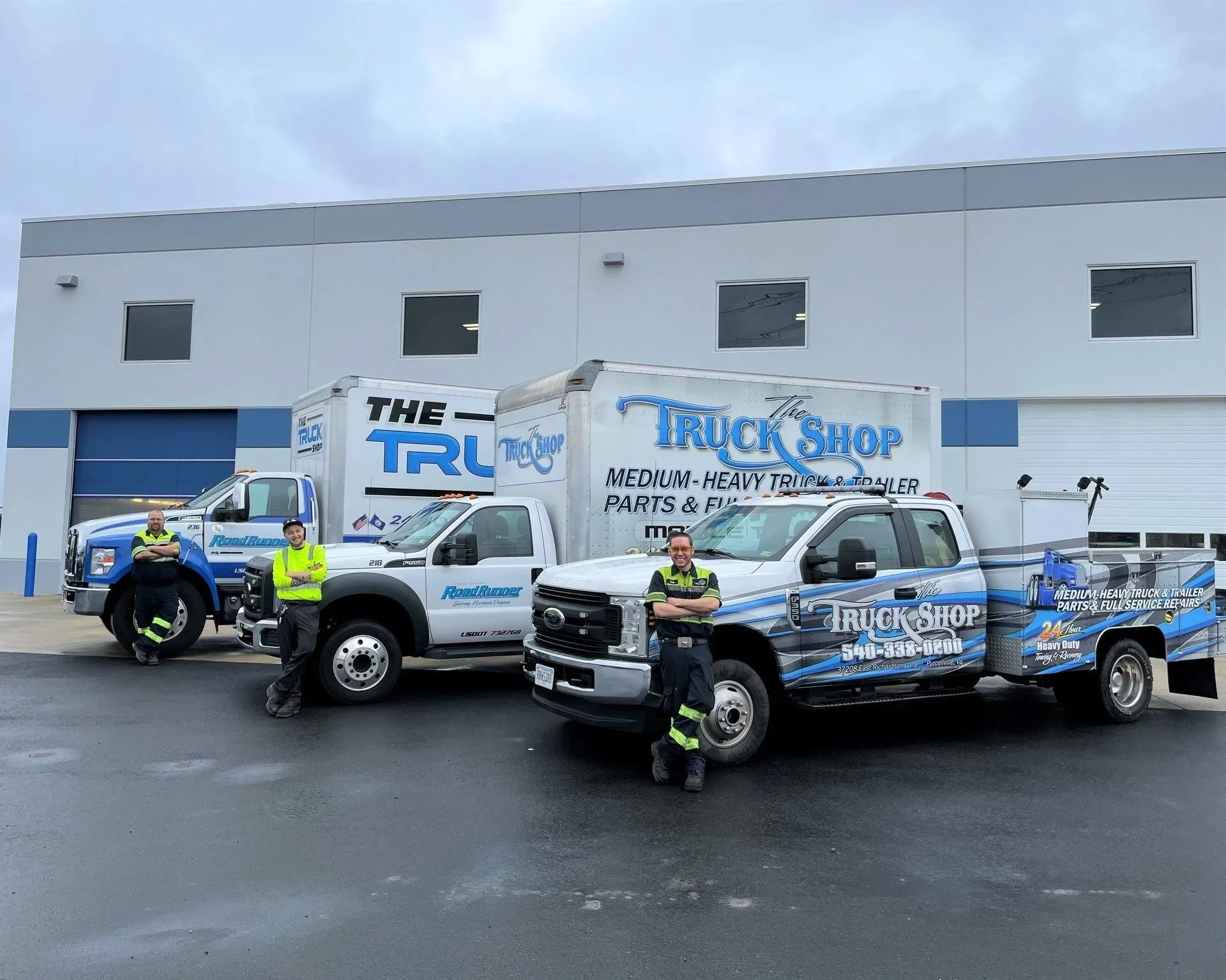 Three workers standing in front of trucks outside a commercial building, wearing high-visibility safety gear.