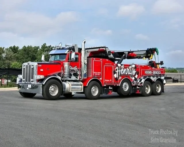 Red tow truck with a crane on the back, parked on an empty lot under a partly cloudy sky.