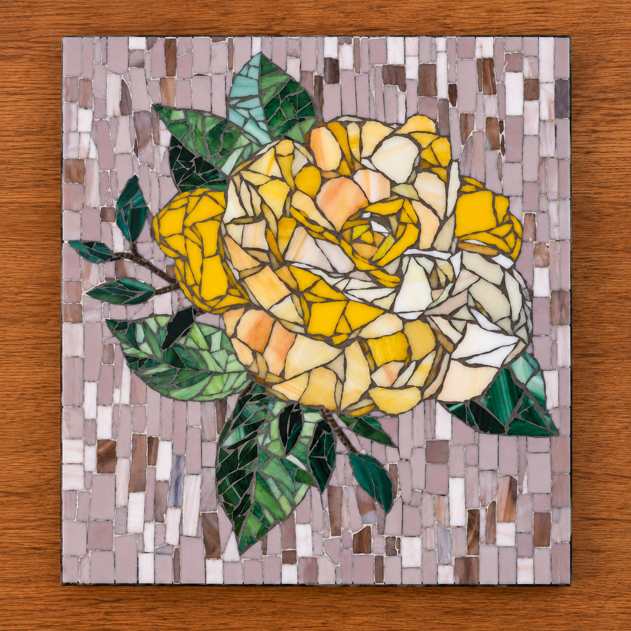 Mosaic artwork of a yellow and cream rose with green leaves on a pinkish-beige tiled background on a wooden surface.