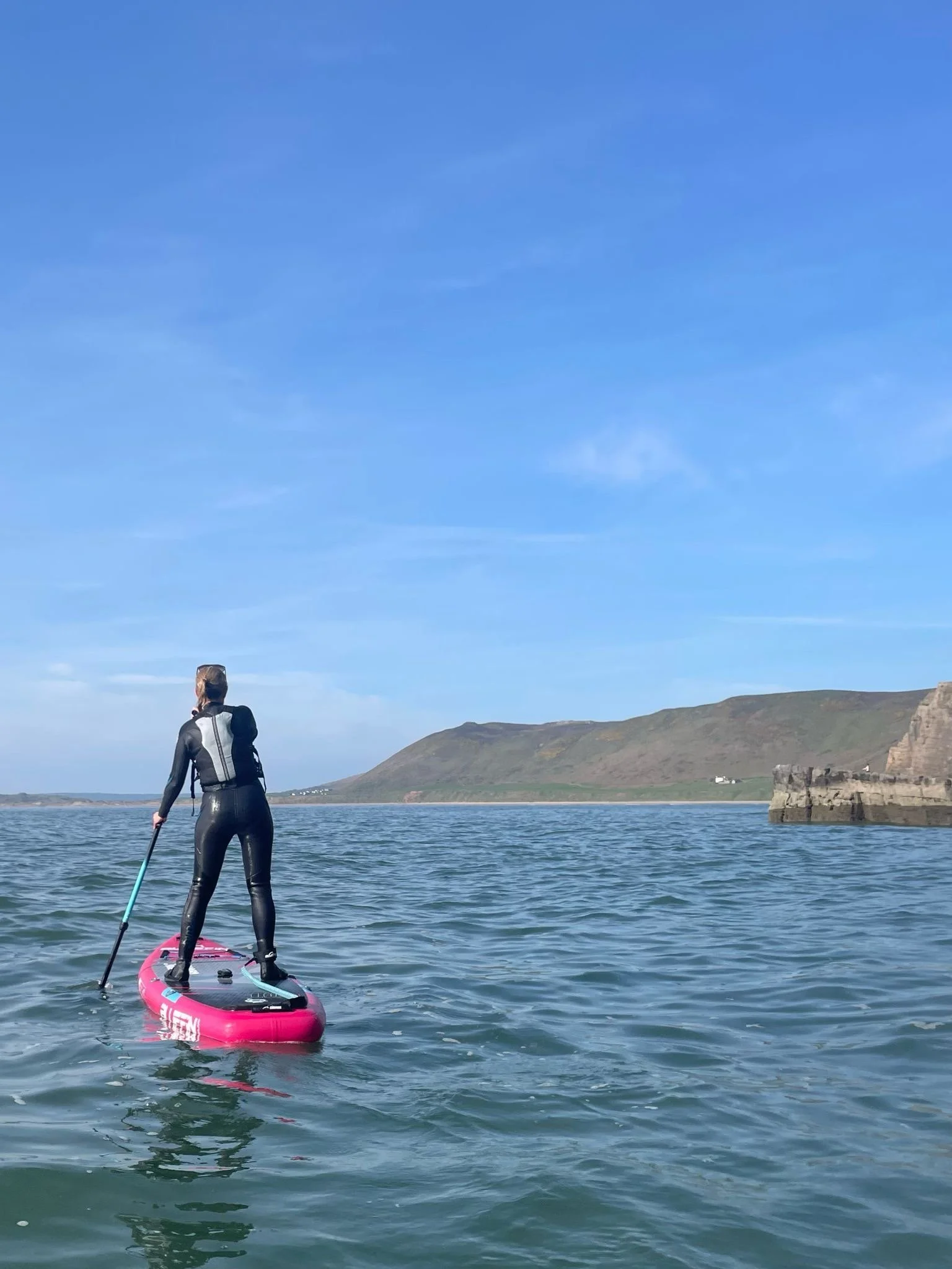 Person paddleboarding on the water during daytime with cliffs and hills in the background.