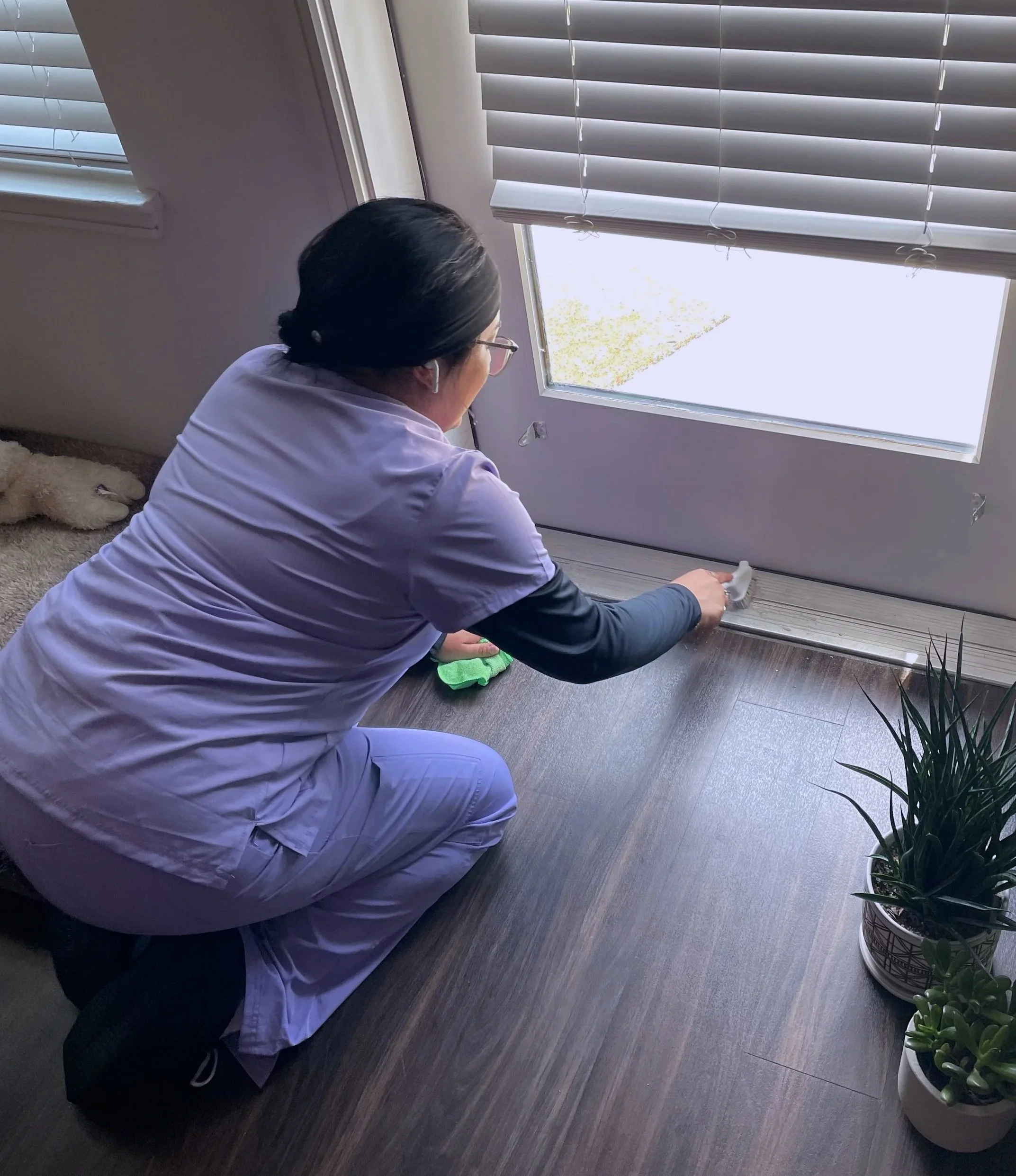 Professional cleaner performing a deep clean, scrubbing the base of a glass door with a detail brush.
