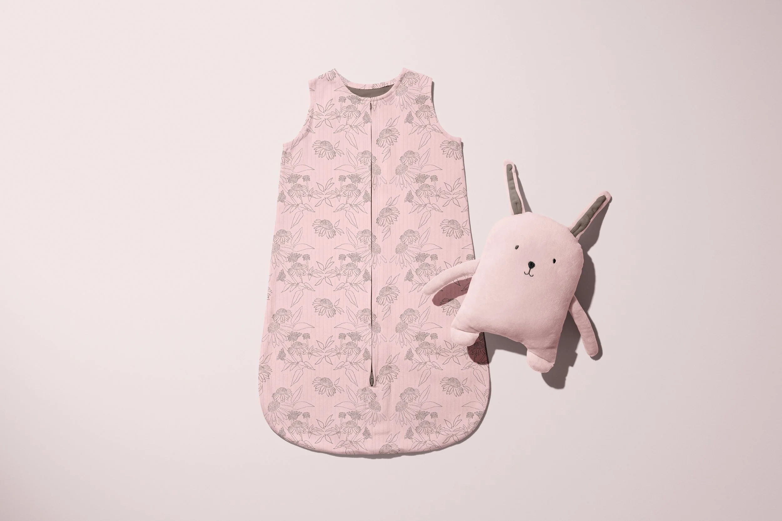 Pink baby sleep sack with floral pattern and a plush bunny rabbit toy.