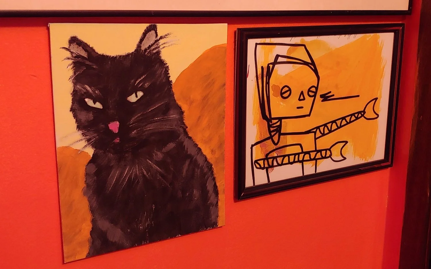 Paintings of a black cat with yellow eyes on the left and a cartoon robot with a square head, holding a spear, on the right, on an orange wall.