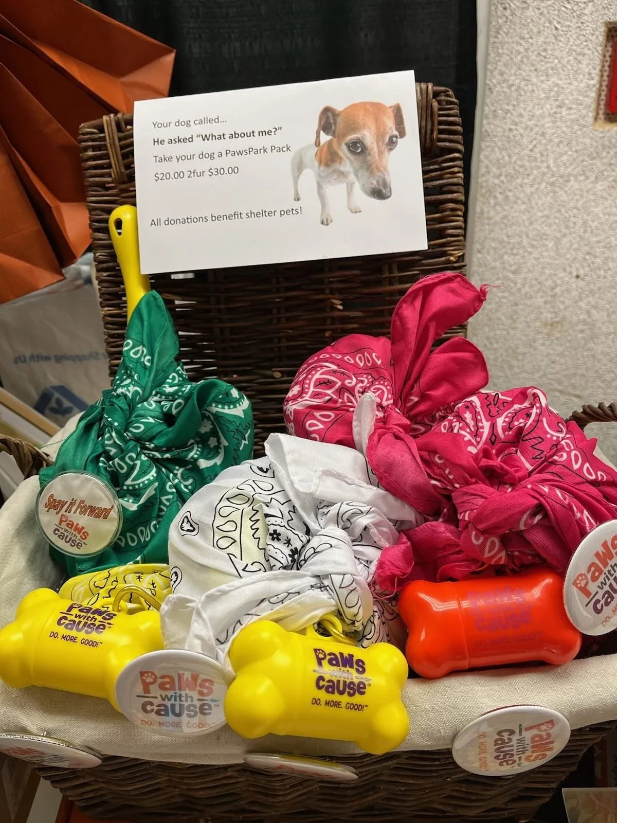 Display of colorful bandanas and chew toys for dogs on a wicker basket with a sign promoting shelter donations.