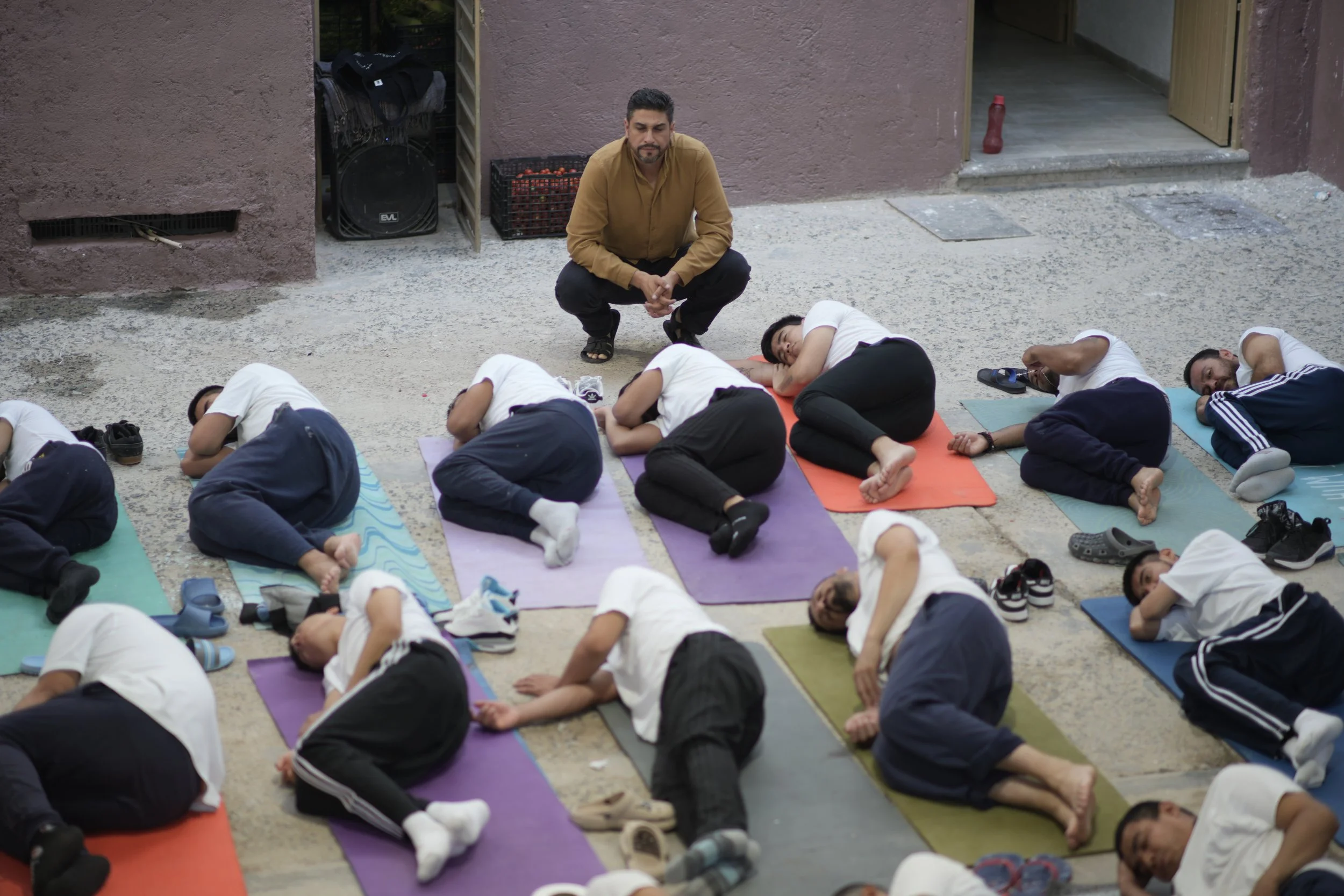 Varias personas haciendo yoga en colchonetas de colores en un patio cerrado, con un Mauro Falfan observando.