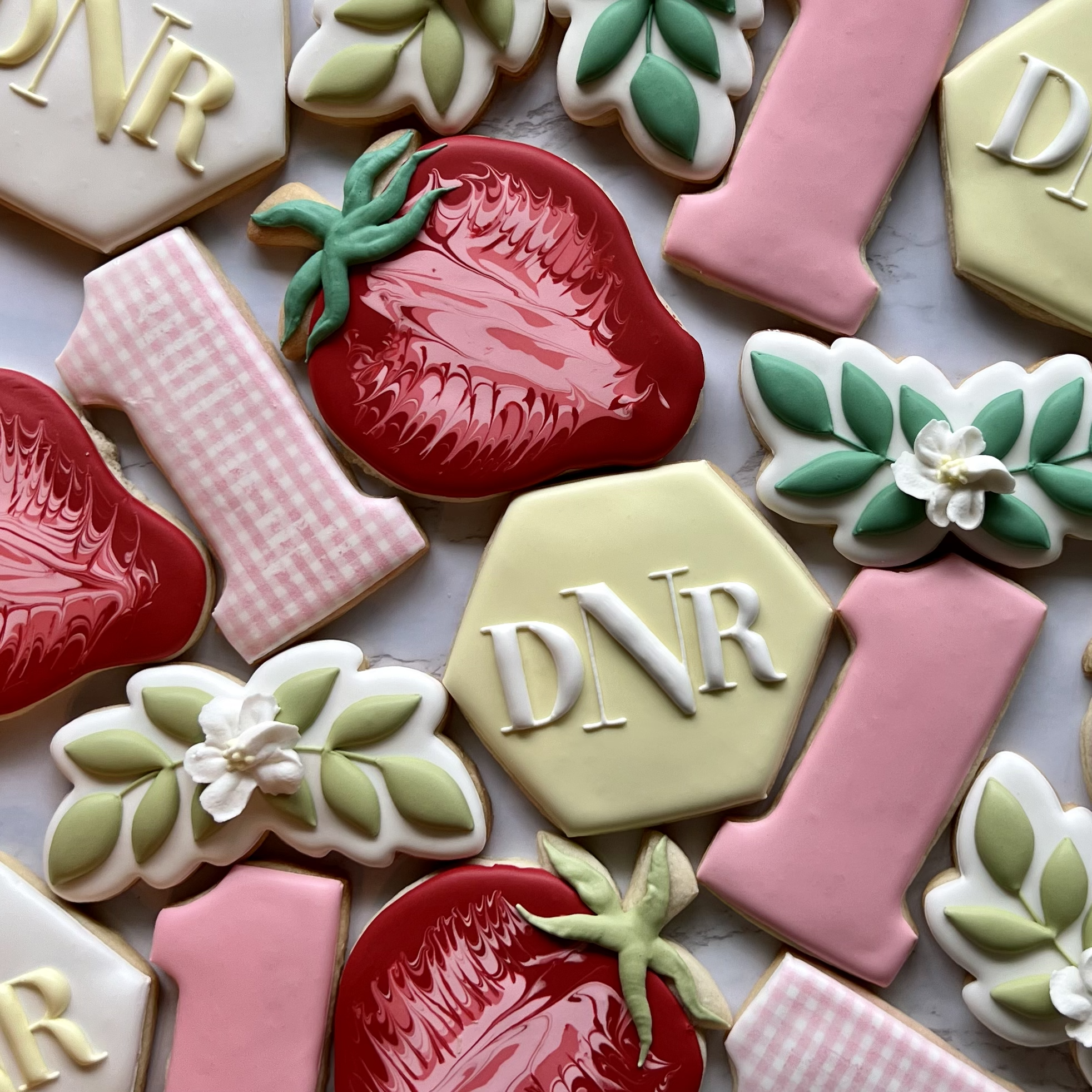Decorative cookies with floral, strawberry, and mongram designs in pastel pink, yellow, green, white, and red colors.