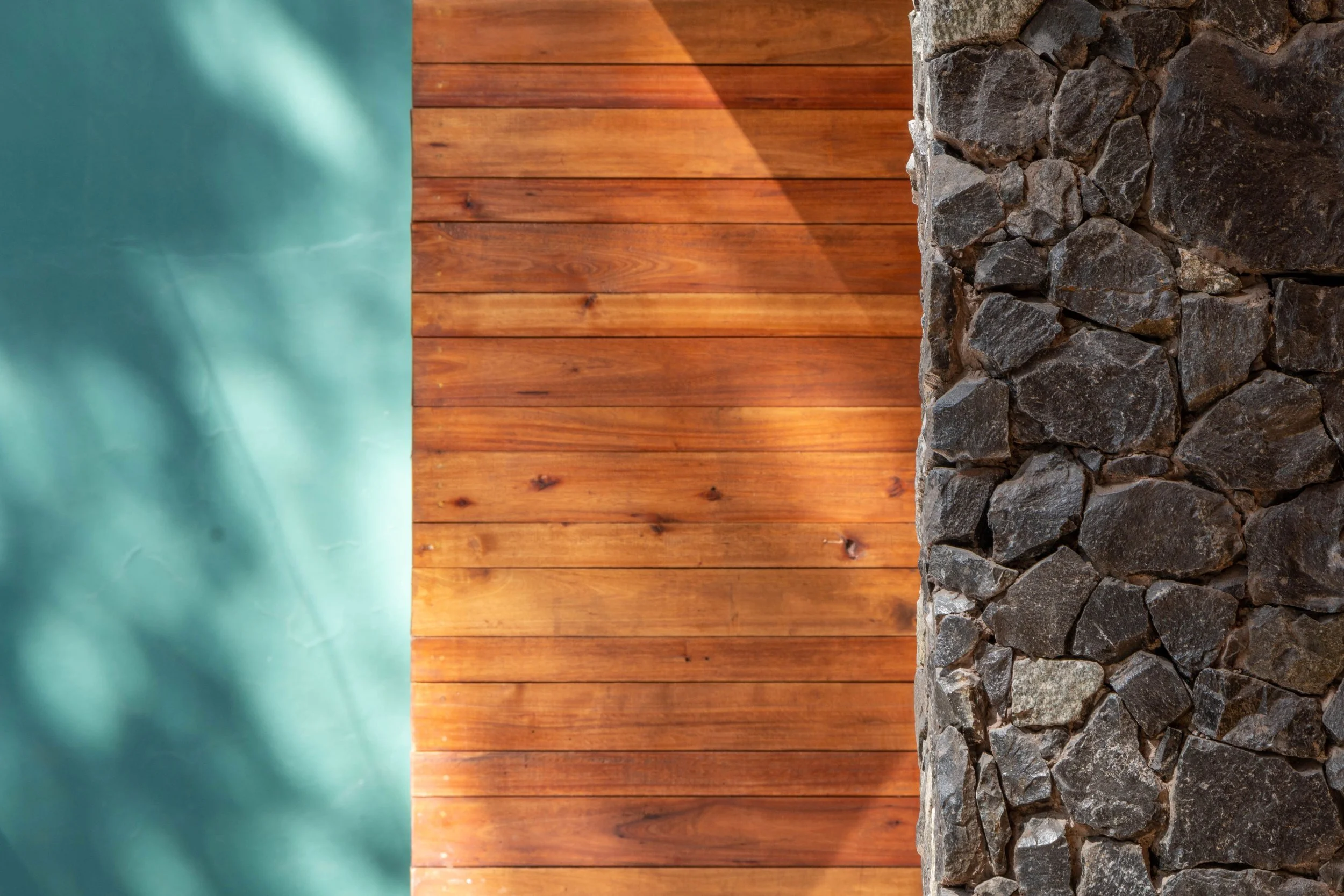 Vista lateral de una pared de madera de color marrón, con una parte de piedra y una pared de color verde al fondo