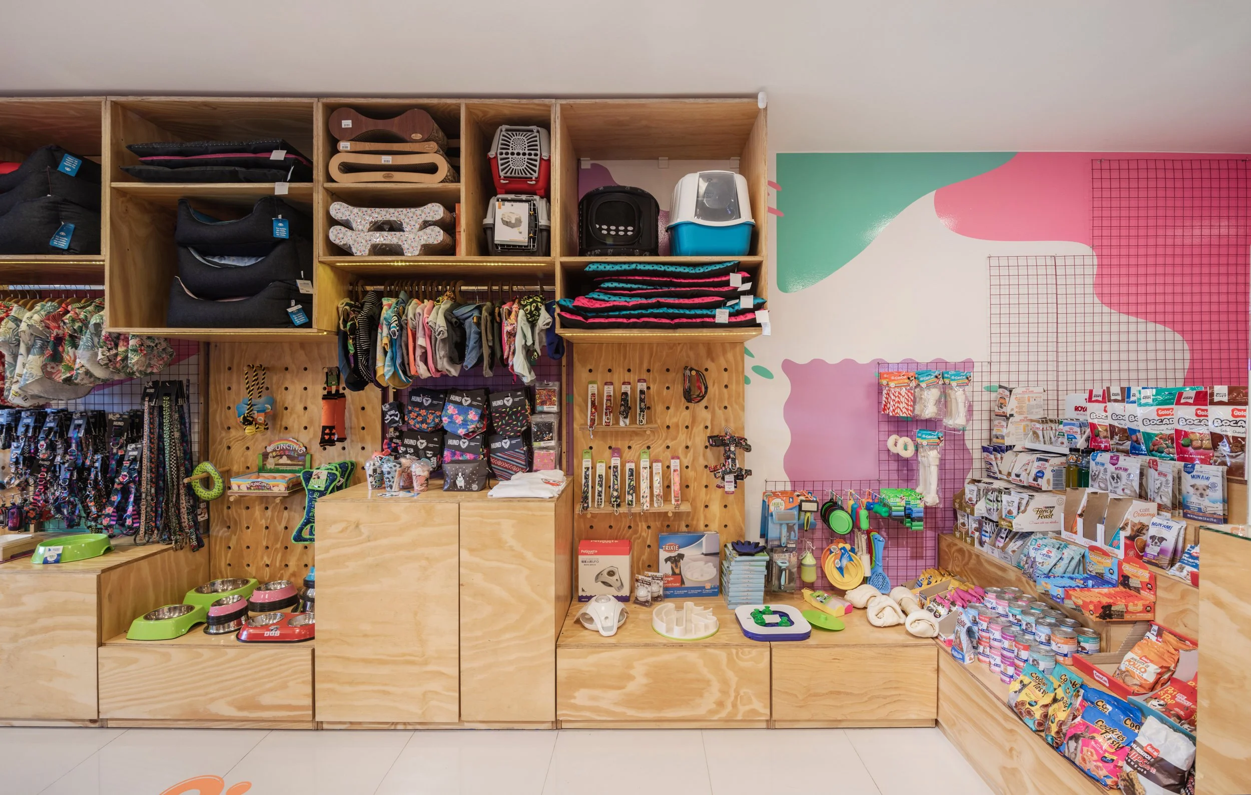 Sección de tienda de mascotas con alimentos, juguetes, accesorios y camas para animales en anaqueles de madera.