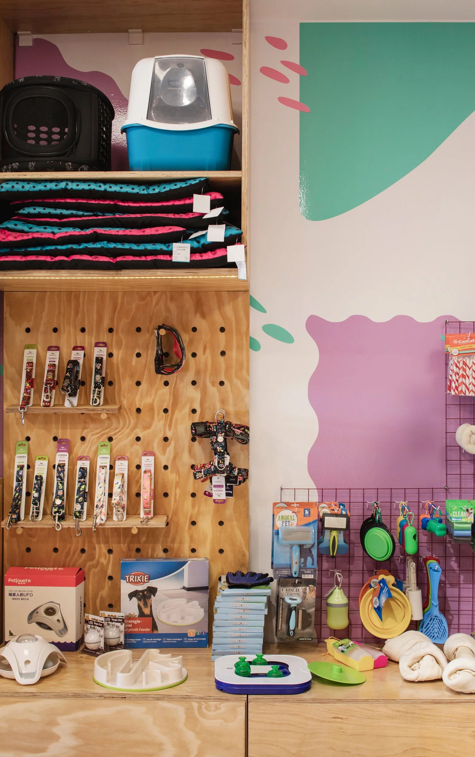 Se muestran accesorios y productos para mascotas, incluyendo collares, juguetes, productos de higiene y muebles en una tienda para animales.