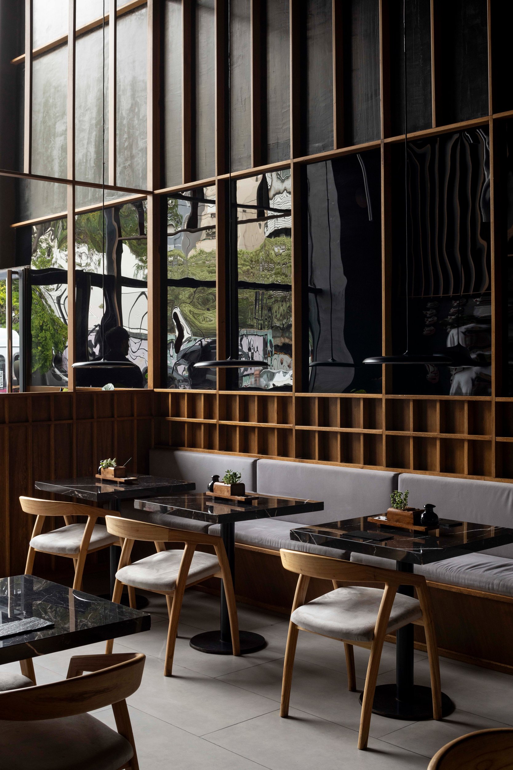 Interiores de un restaurante moderno con sillas de madera, mesas de piedra negra y paredes de madera con espejo
