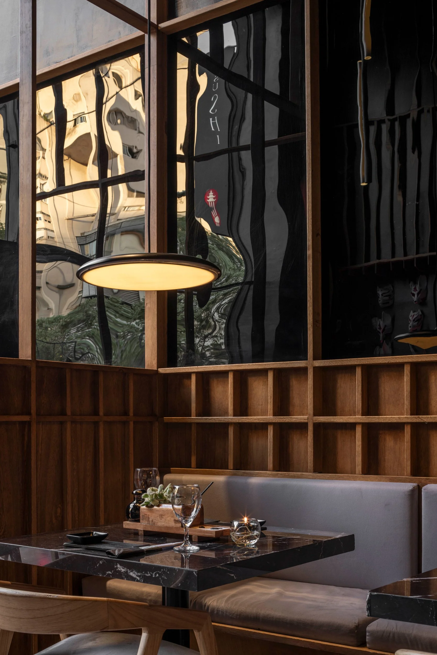Interior de restaurante con paredes de madera, un espejo ondulado, lámparas circulares y una mesa con copas y velas.