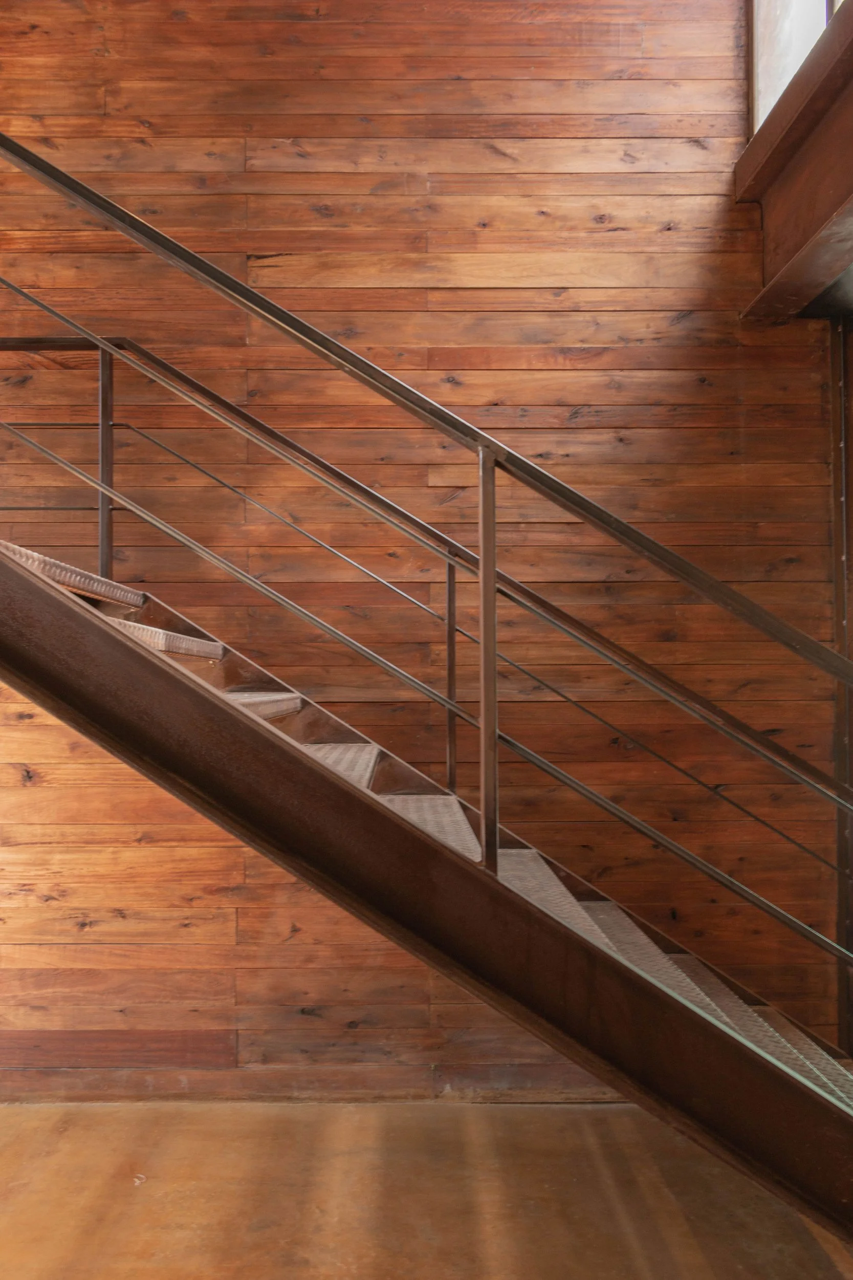 Escalera de metal con pasamanos junto a paredes y piso de madera natural.