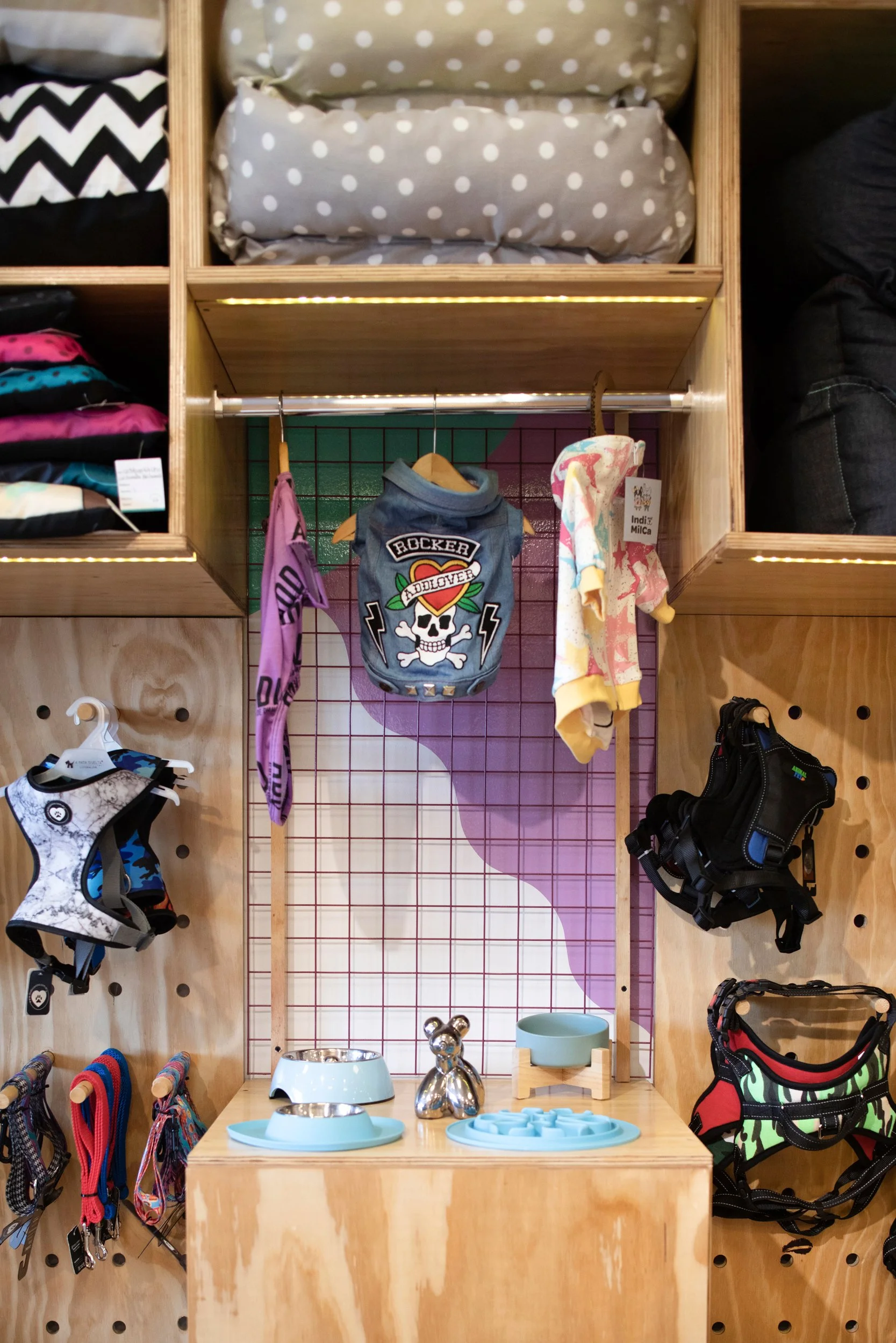 Sección con accesorios para mascotas y ropa infantil, incluyendo collares, ropa, camas para perros y juguetes, en una tienda
