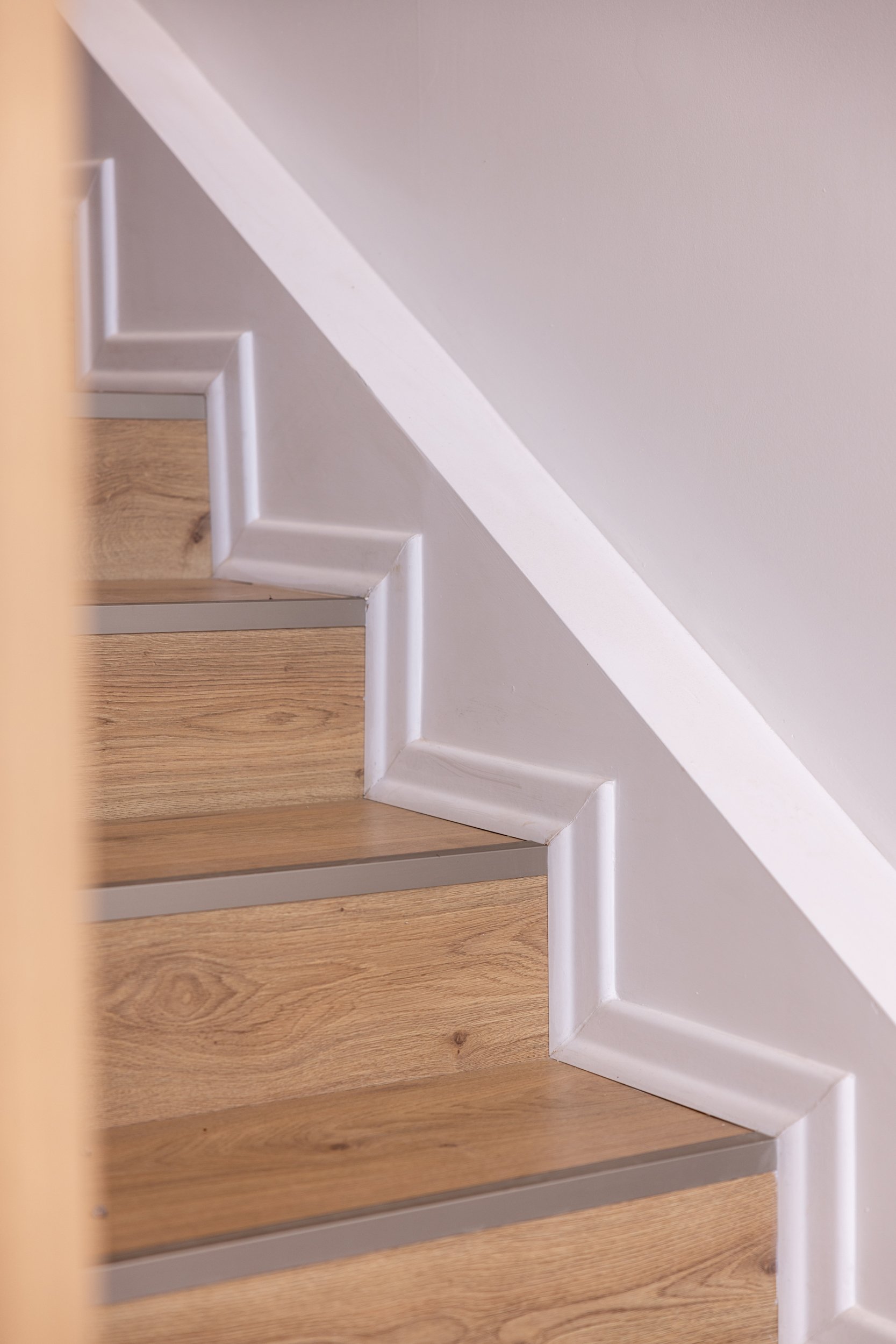 Escalera de madera con barandilla blanca y moldura decorativa blanca en la esquina.