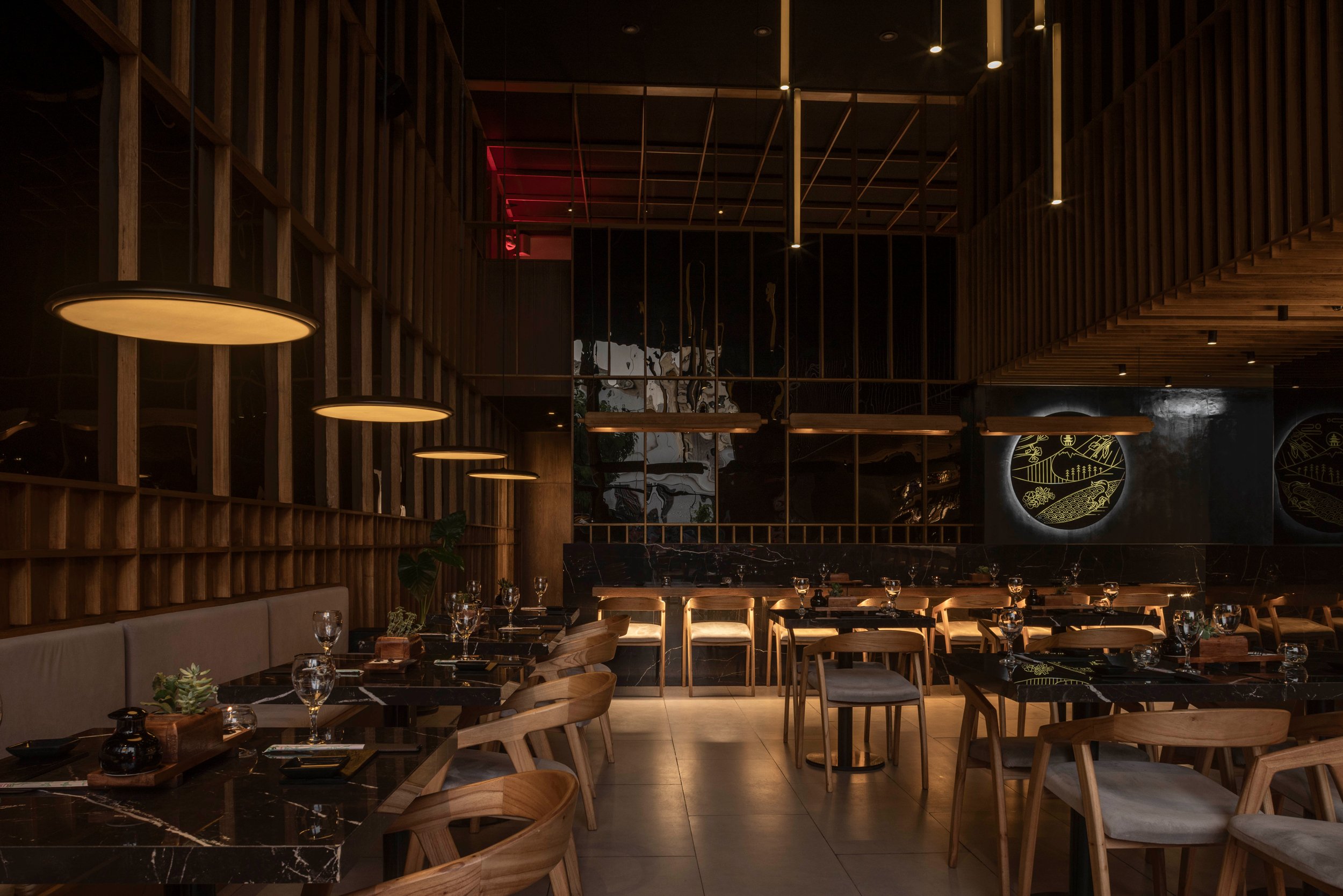 Interior de restaurante elegante con mesas de mármol negro, sillas de madera, iluminación cálida, paredes de madera y decoraciones modernas.