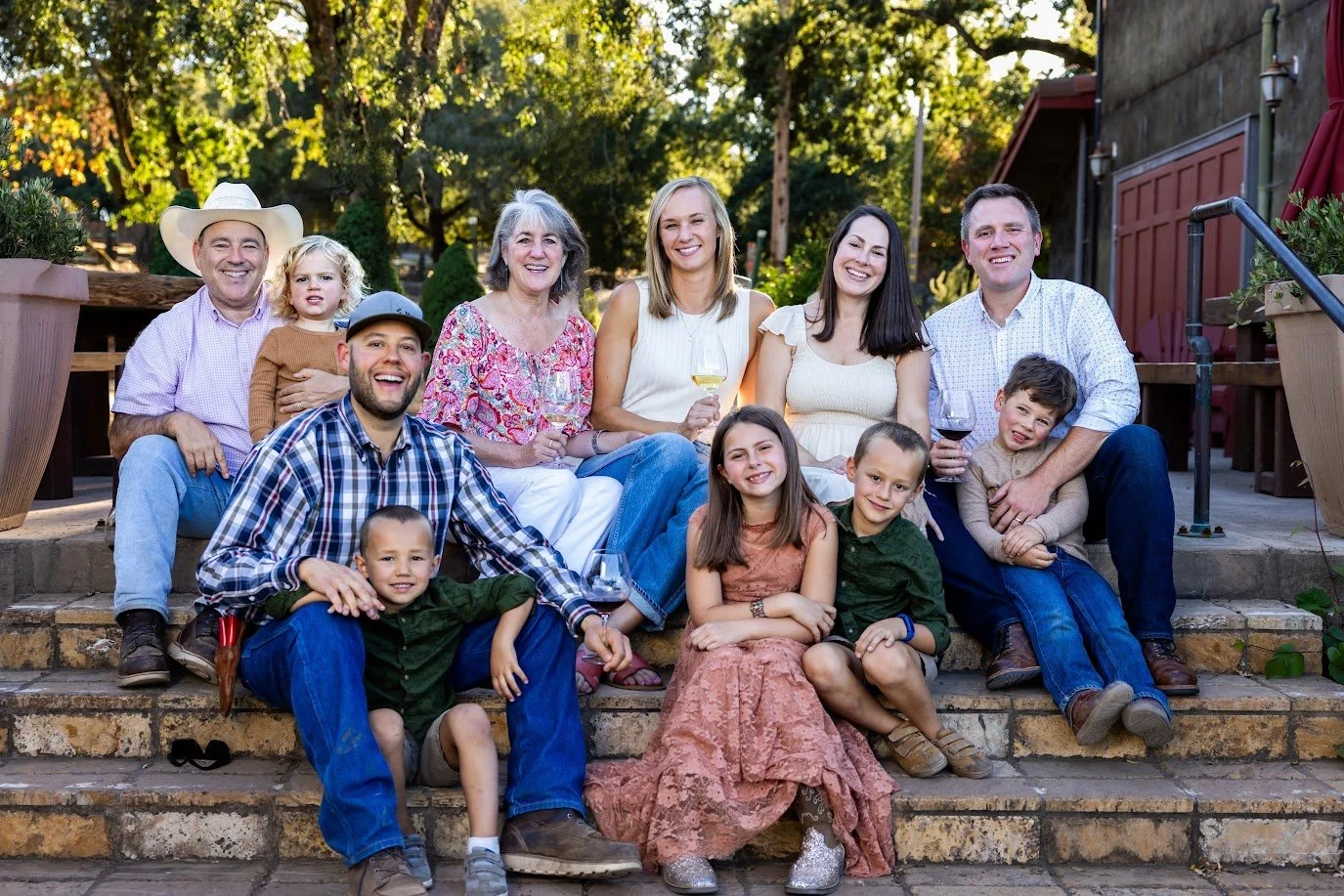 The Gracianna Winery family sitting on outdoor stairs, smiling and enjoying each other's company, with trees and a building in the background.
