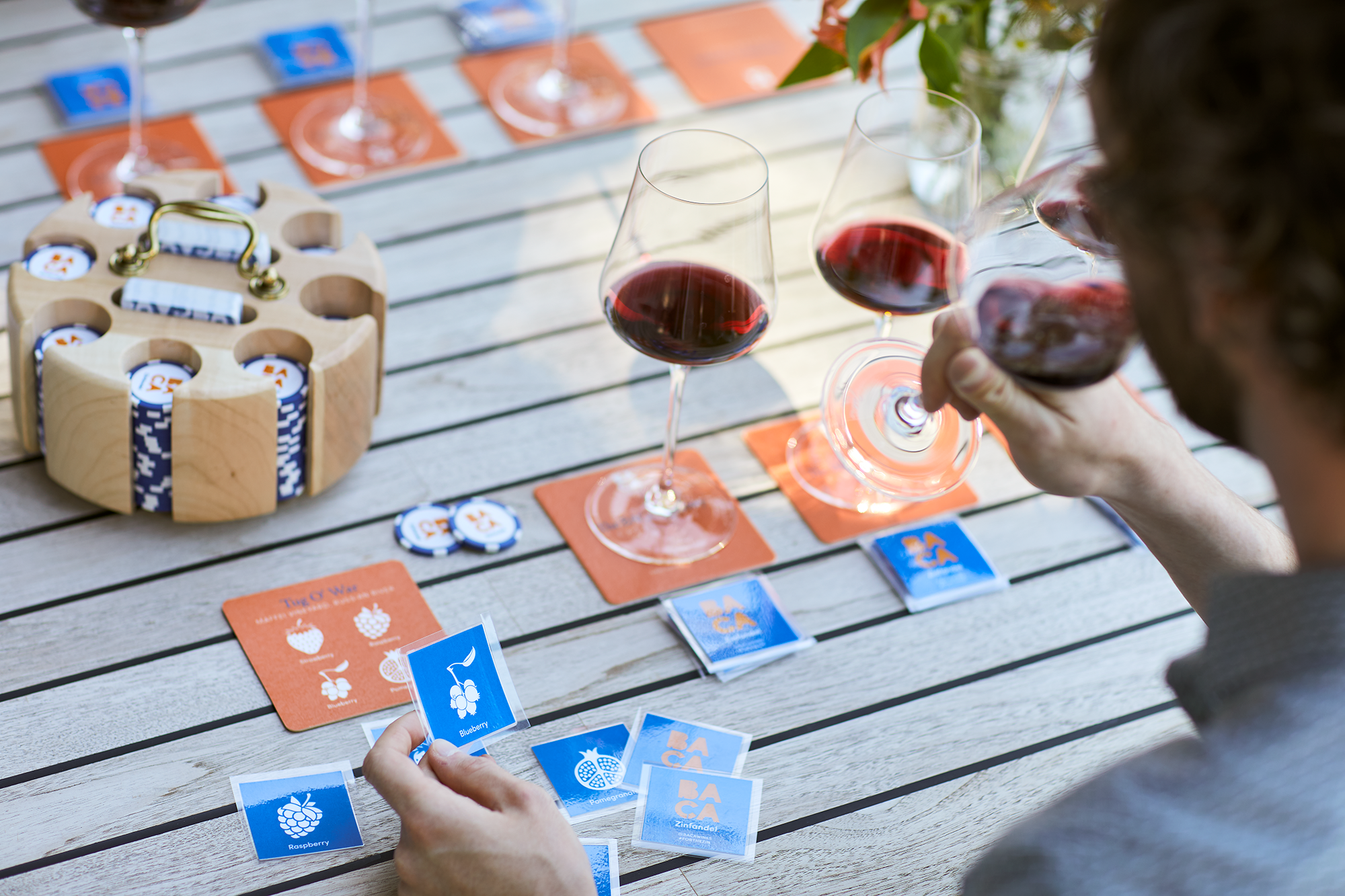 People playing a card game with a spread of fruit names and images on cards, with a glass of red wine on a wooden table.