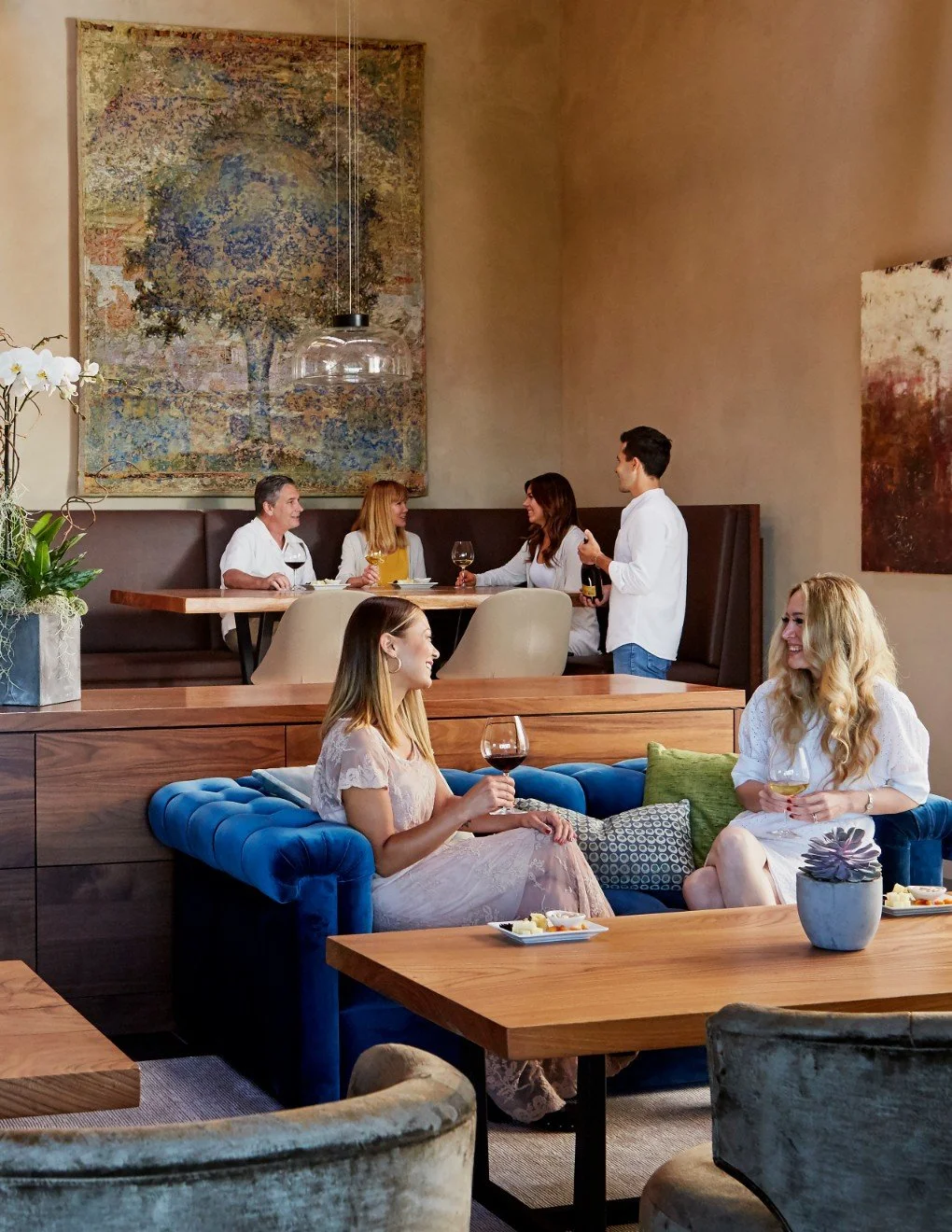 People socializing and enjoying wine in a modern, upscale restaurant with abstract art on the walls and stylish furniture.