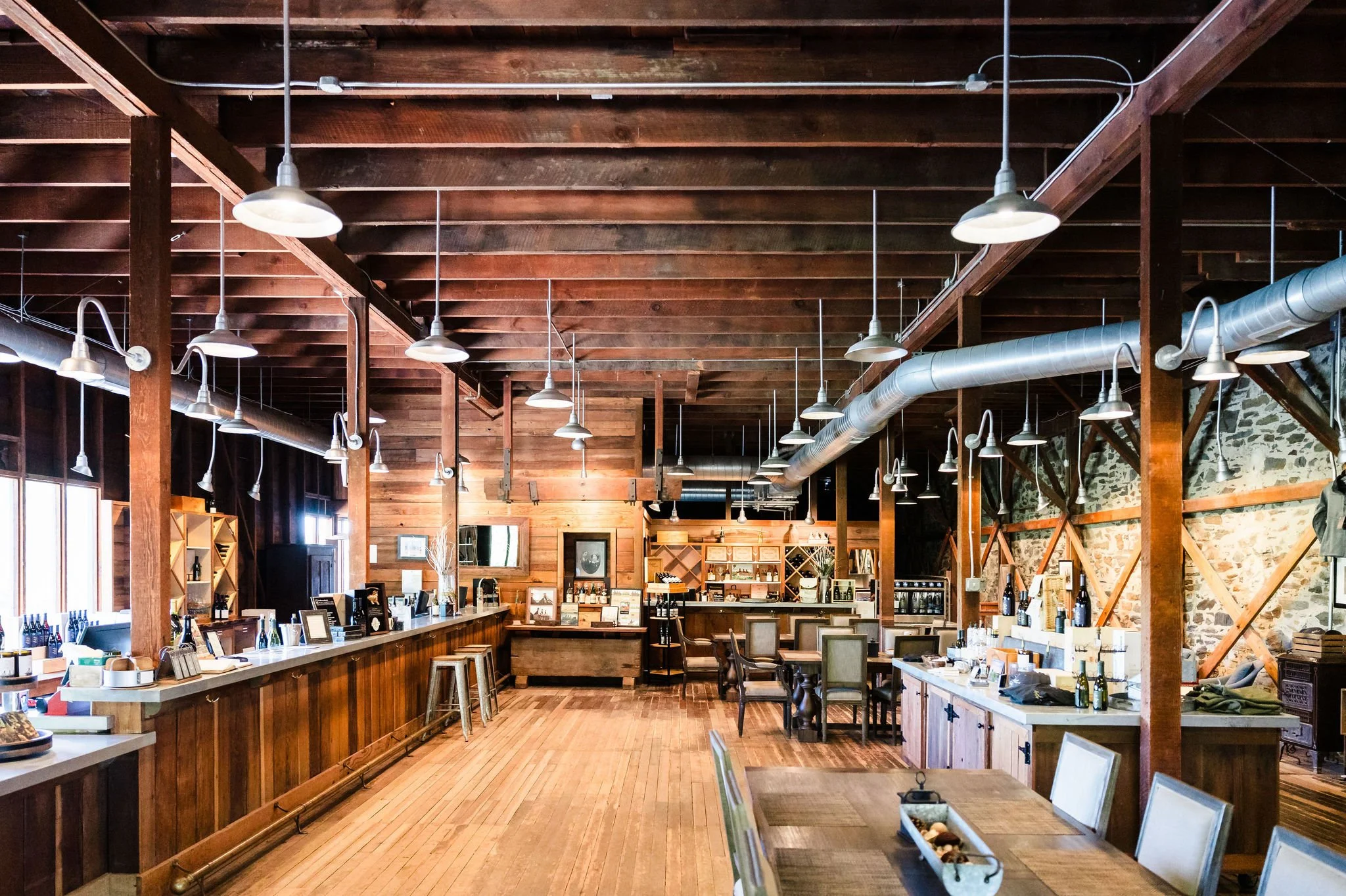 Inside view of Landmark at Hop Kiln Estate with wooden beams, hanging lights, and a long wooden counter with wine bottles, pictures, and decor.