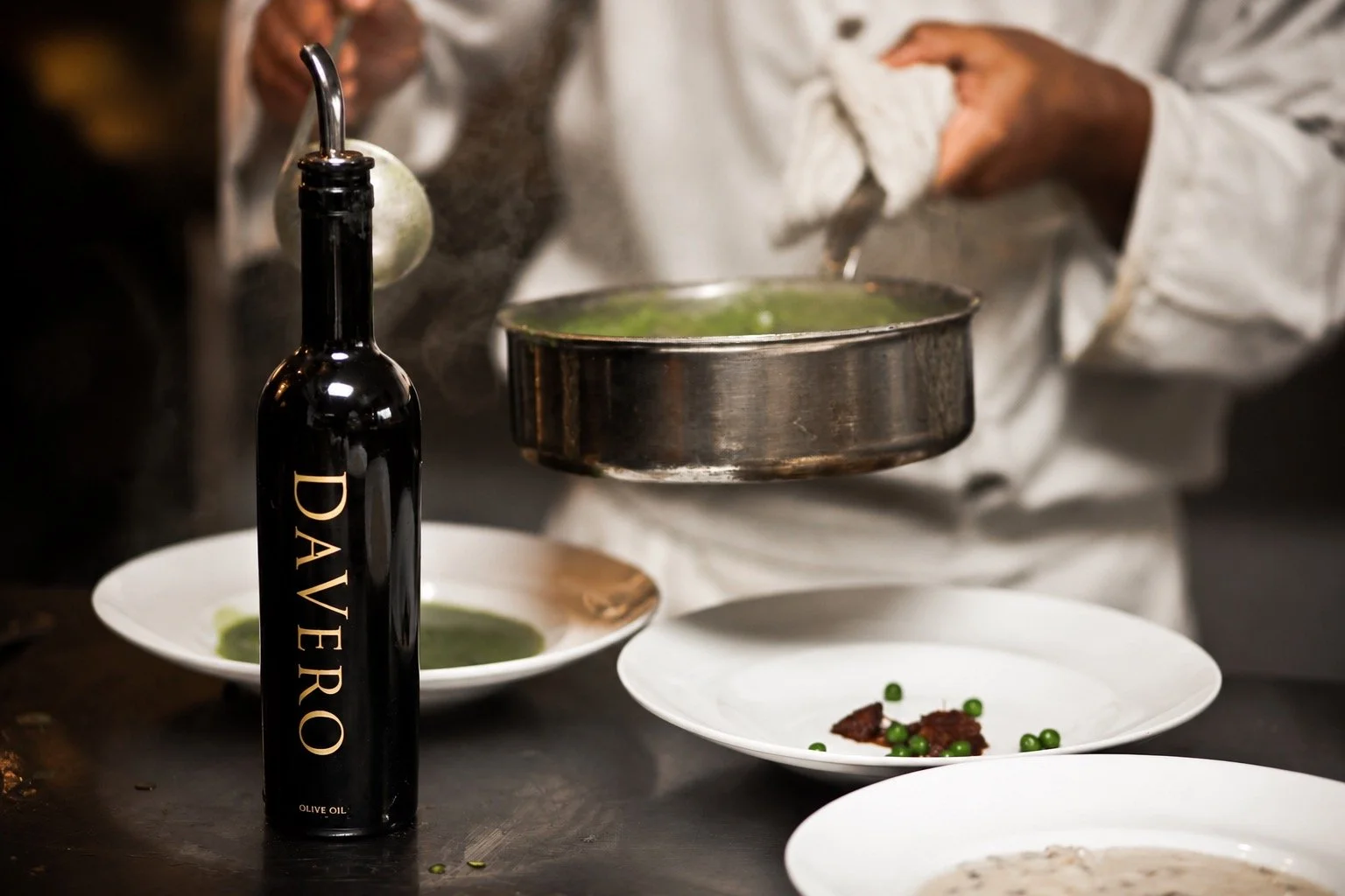 Chef preparing dishes in a kitchen, with plates of food, a bottle of olive oil, and cooking utensils on the counter